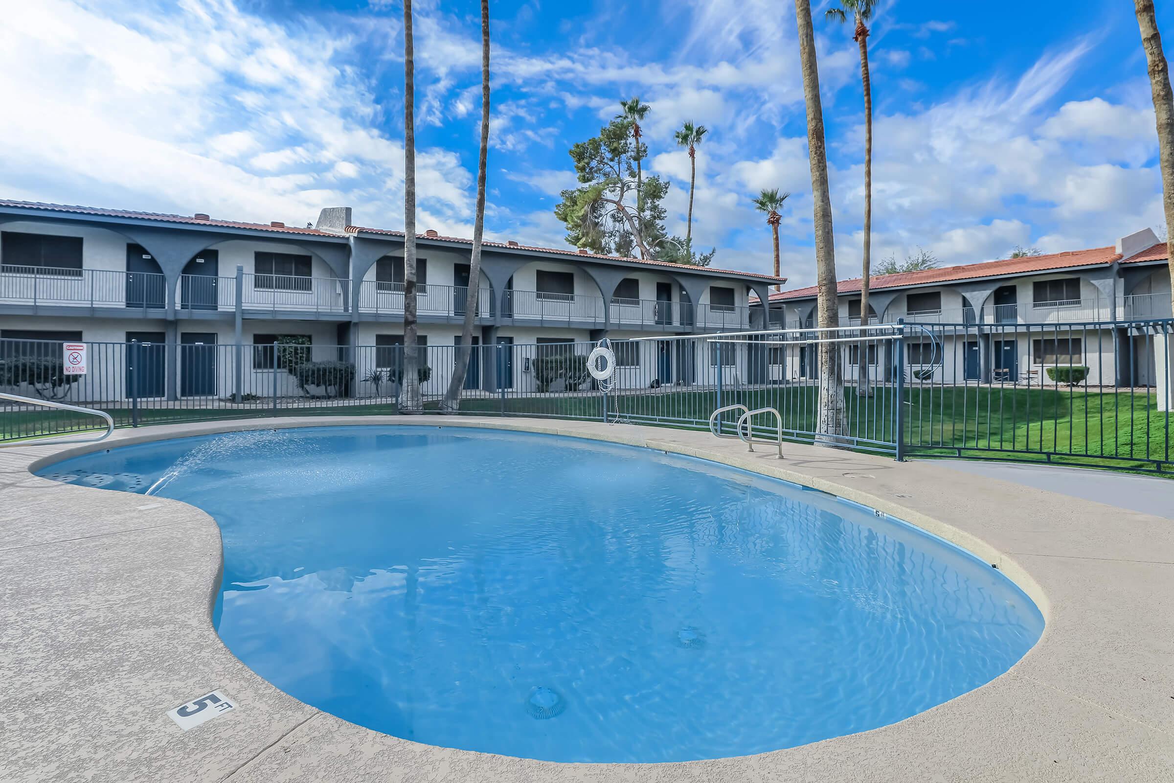 Large outdoor pool with view of a 2 story apartment building behind it