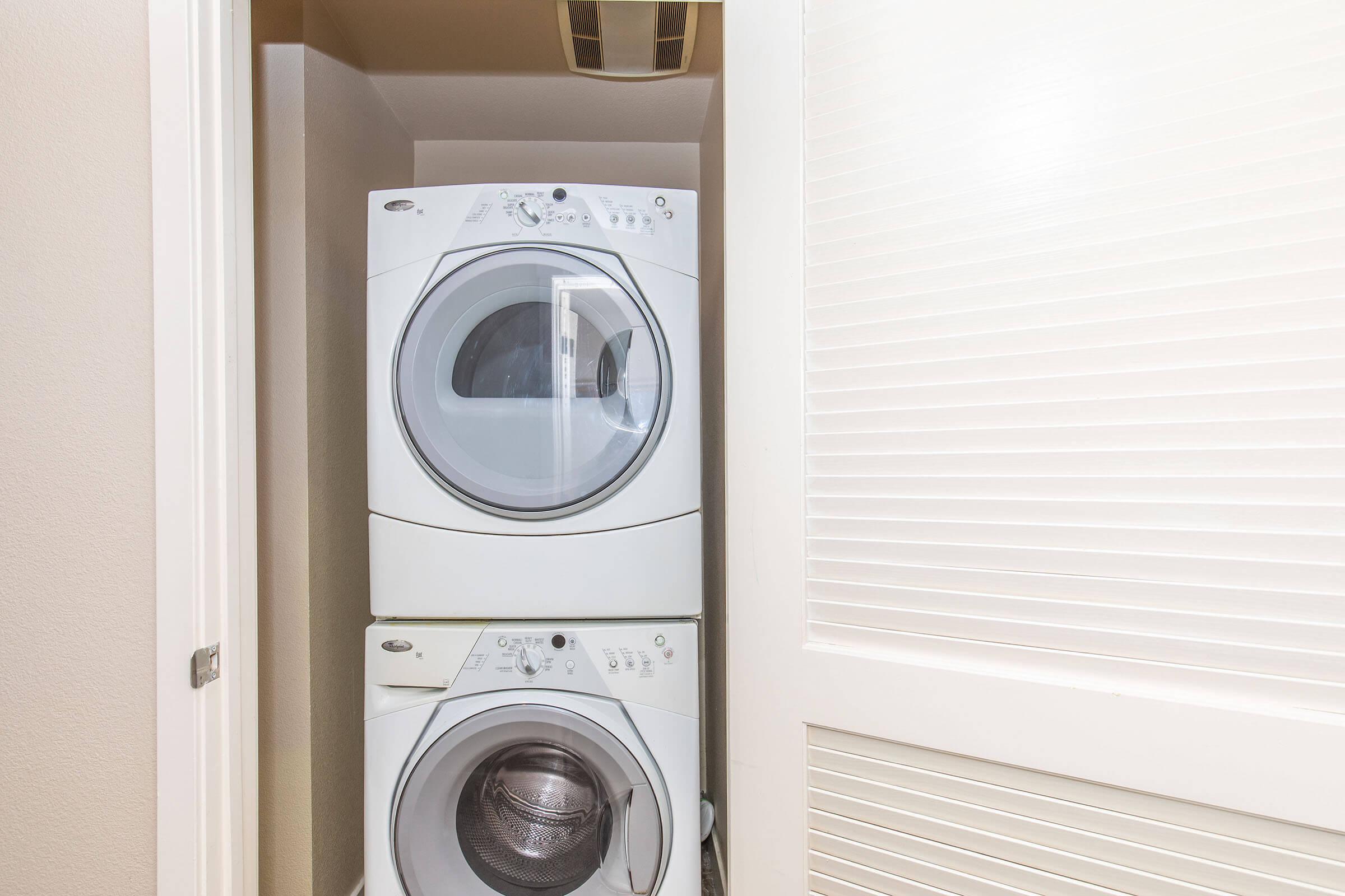 A compact laundry closet featuring a stacked washer and dryer. The appliances are white, and the space is enclosed by a light-colored door with horizontal slats. The interior appears clean and organized, suitable for laundry tasks.