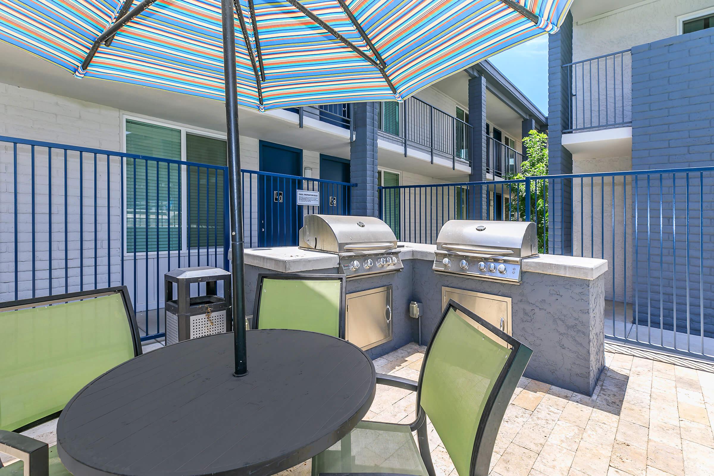 Outdoor patio dining set with large shaded umbrella next to 2 bbq grills at Rise Canyon West apartments in Phoenix