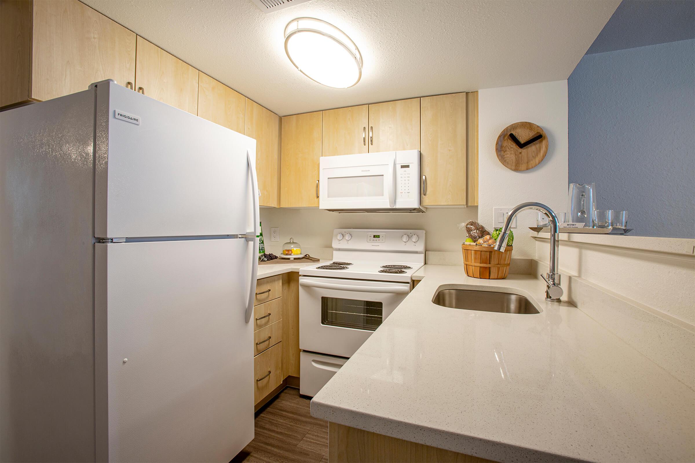 Phoenix, AZ apartment kitchen with large quartz counter-space, light wood cabinets, and white appliances