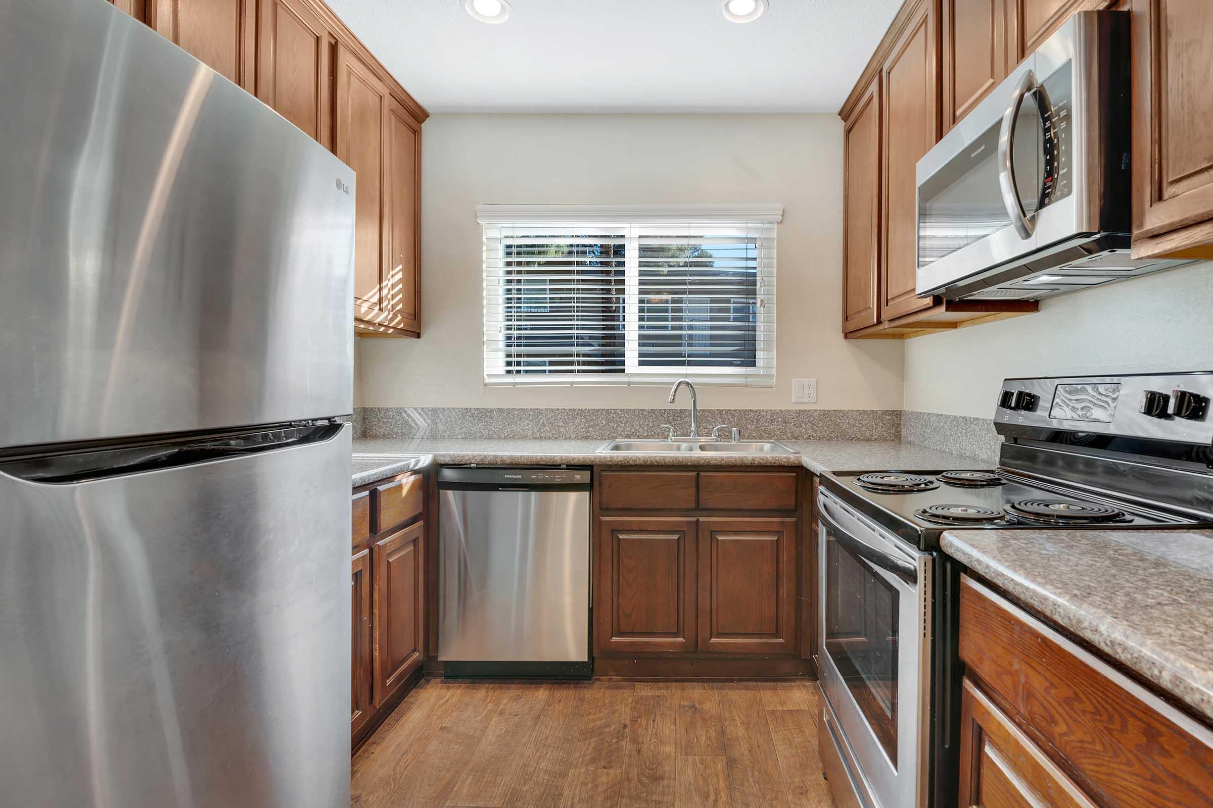Modern kitchen featuring stainless steel appliances including a refrigerator, dishwasher, and oven. The cabinetry is dark wood, complemented by a granite countertop. A window provides natural light, and the space is equipped with a dual sink and built-in stovetop.