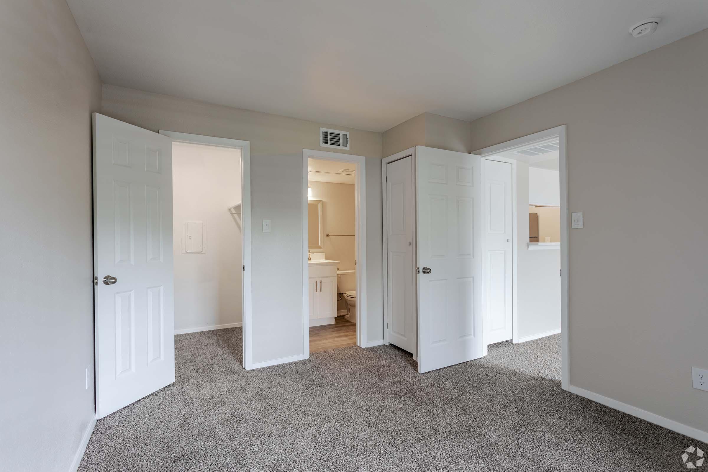 View of a room featuring multiple doorways leading to different areas. The walls are painted a neutral color, and the floor is carpeted. A small bathroom is visible through one of the doors, showcasing a bright and clean interior. Natural light fills the space, enhancing the welcoming atmosphere.
