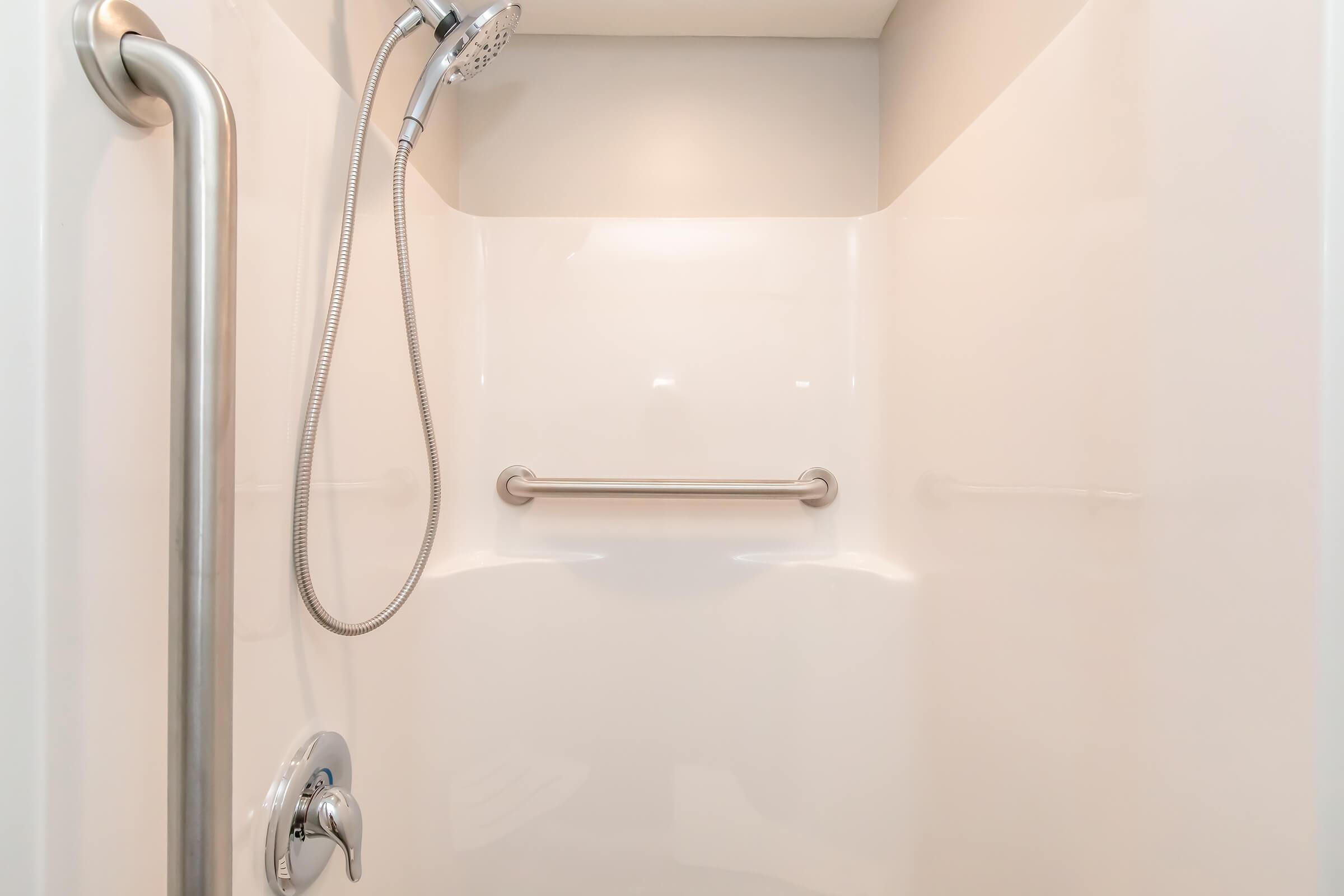 A clean, modern shower stall featuring white walls, a handheld showerhead, and a grab bar for safety. The design is minimalist and bright, creating an inviting shower space.