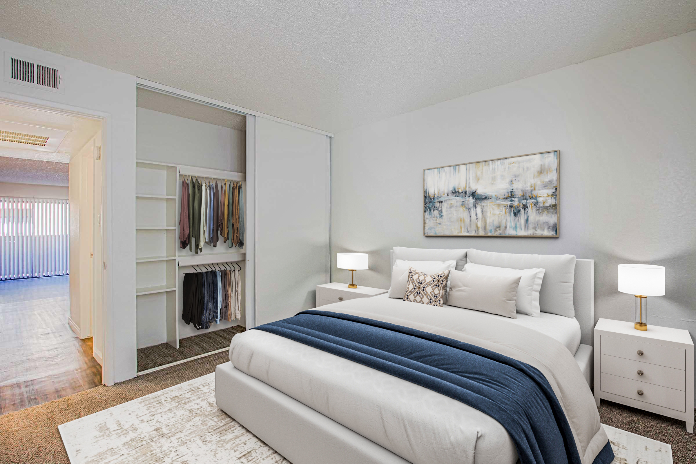 A modern bedroom featuring a neatly made bed with white and navy bedding, two bedside tables with lamps, and a large abstract painting on the wall. The closet with organized clothing is visible in the background, and light streams in from a window, creating a bright and inviting atmosphere.
