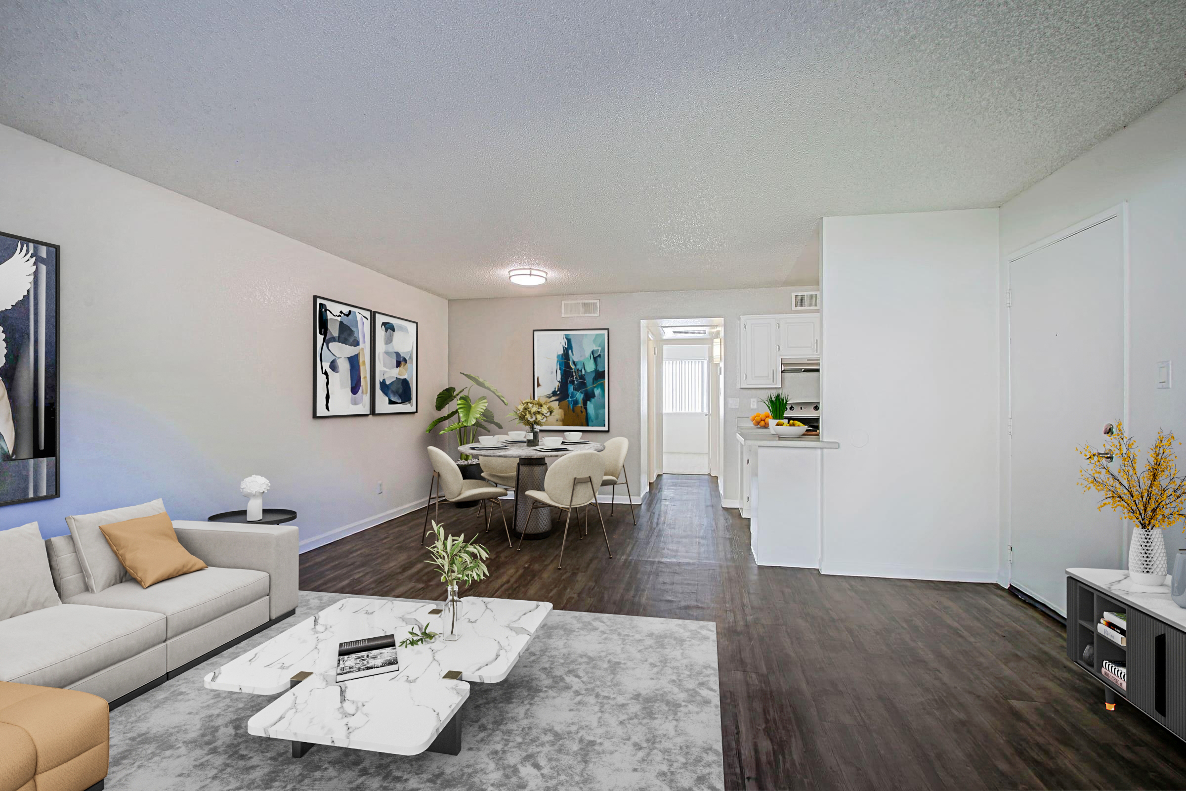 A modern living space featuring a light gray sofa and a marble coffee table on a textured rug. The room is adorned with abstract wall art and includes a dining area with a table and chairs. A kitchen is visible in the background, and natural light comes through a door leading outside.