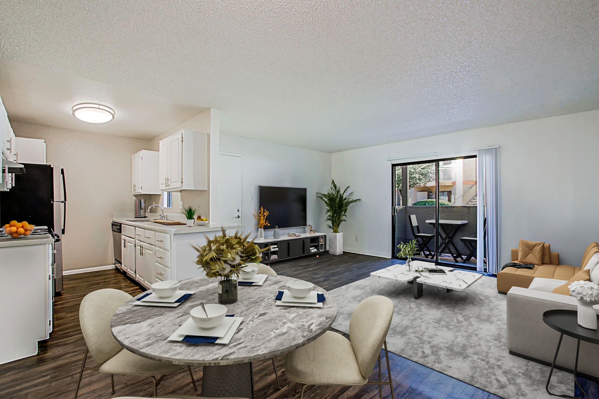 A modern living space featuring a dining area with a round marble table set for four. The kitchen, with white cabinets and black appliances, is visible in the background. A comfortable beige sofa and a coffee table are in the living room, which has a large window leading to a small balcony, and green plants are decoratively arranged.
