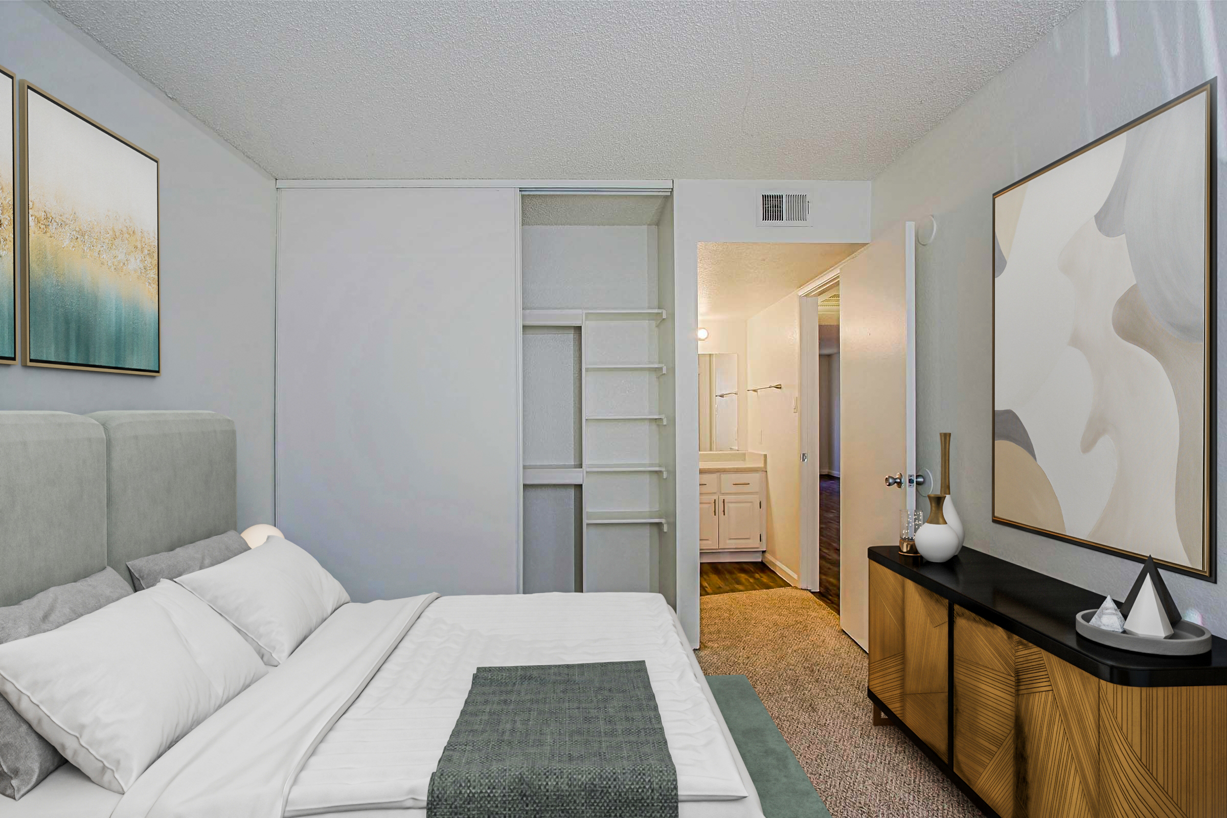 A modern bedroom featuring a plush gray bed with white linens, accented by a light green throw blanket. Adjacent to the bed is a stylish nightstand with decorative items. The walls are adorned with abstract art, and a closet is visible, leading to a doorway that opens into a bathroom area.