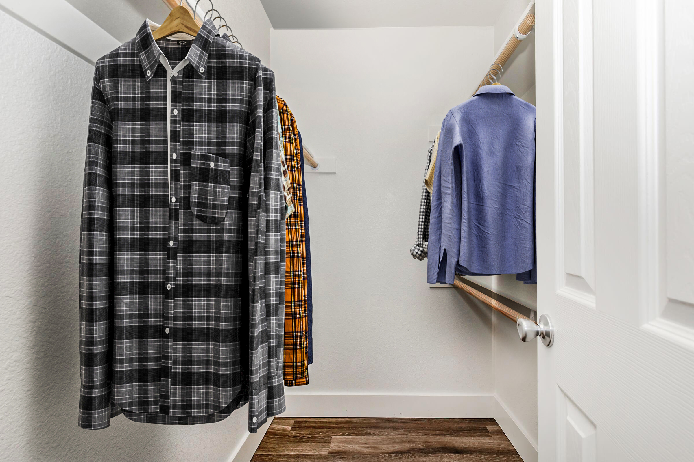 A well-organized closet with several shirts hanging on wooden hangers, including a black and white checkered shirt and a blue shirt, against a plain white wall. The floor is wooden, creating a clean and modern aesthetic.