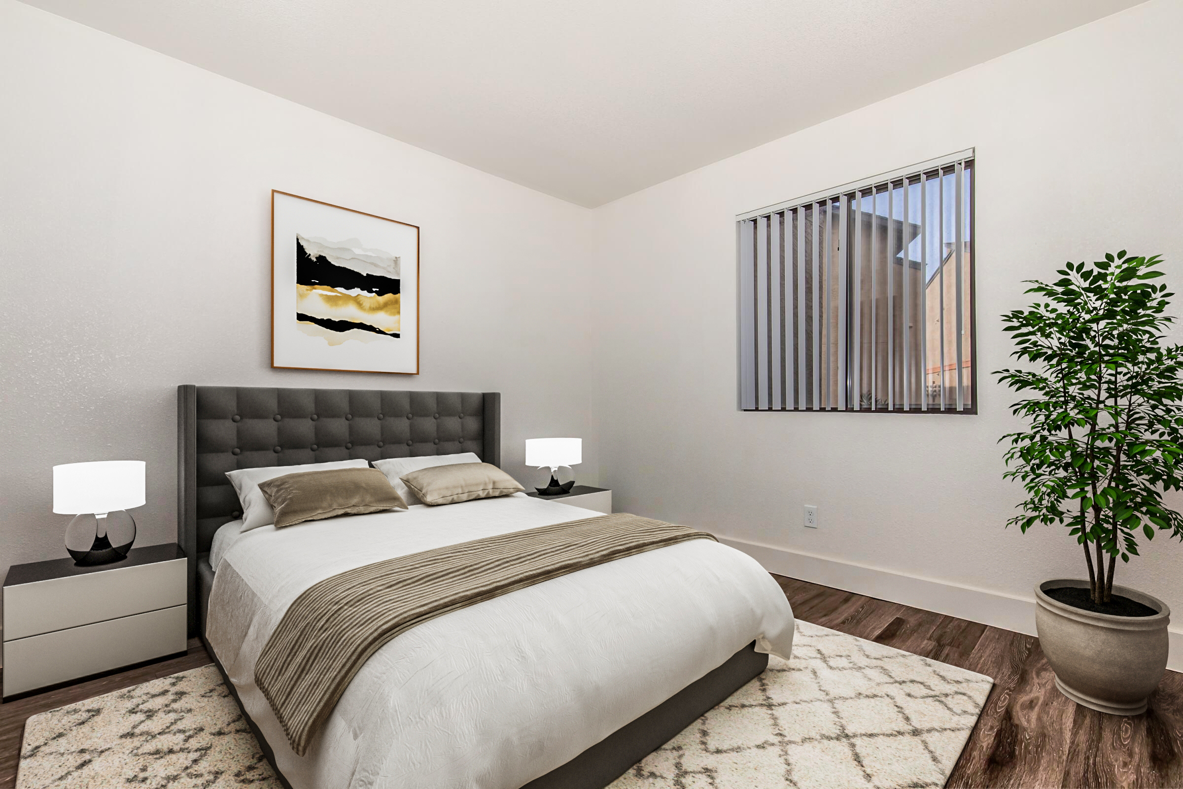 A modern bedroom featuring a queen-sized bed with a tufted gray headboard, two bedside lamps, and a piece of abstract art on the wall. There’s a window with blinds allowing natural light, and a small potted plant adds a touch of greenery. The floor is wooden, and a textured area rug is placed under the bed.