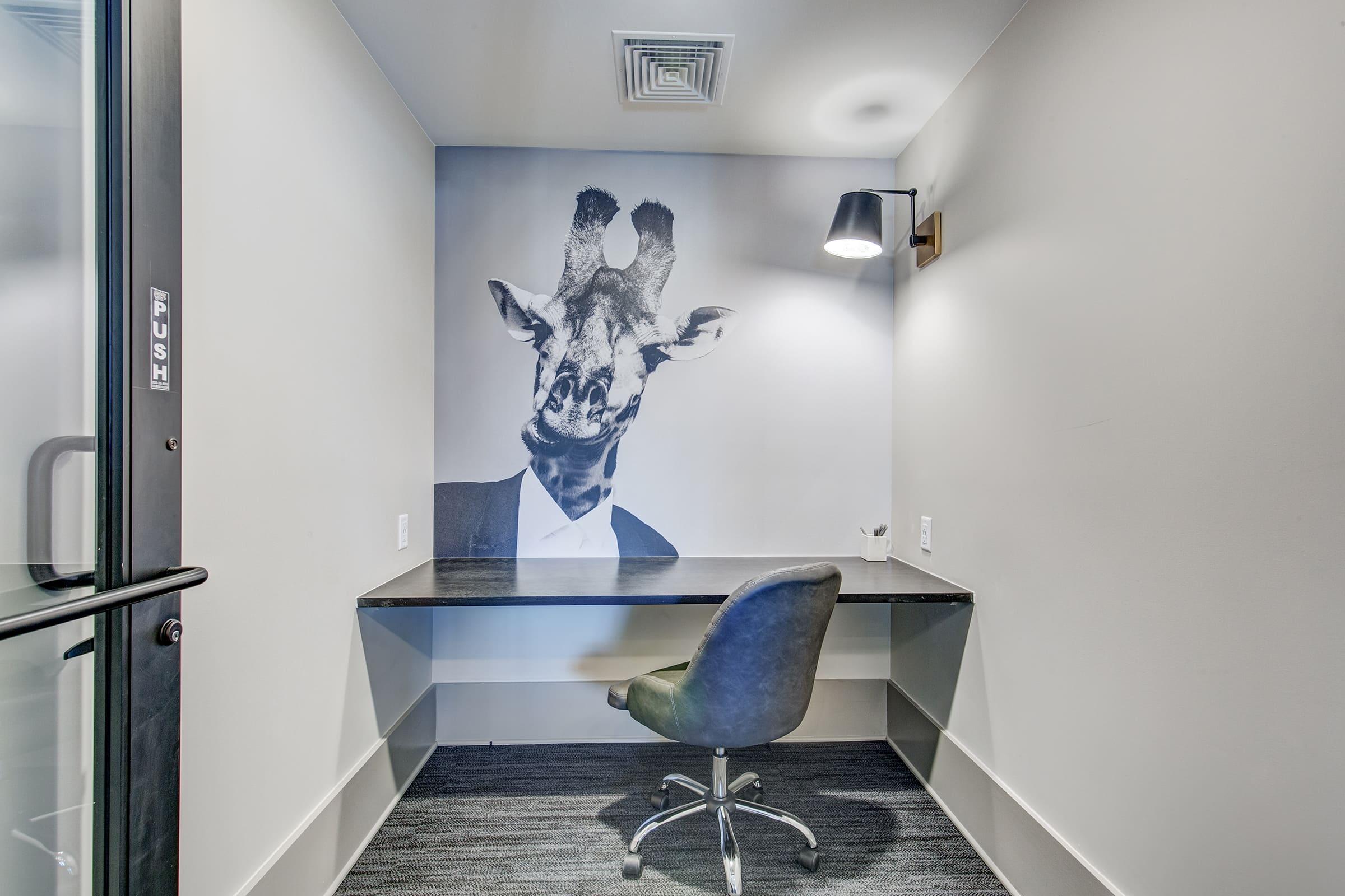 A modern workspace featuring a wall art depicting a giraffe wearing a suit. The desk is sleek and simple, accompanied by a comfortable chair, while a spotlight illuminates the area, creating an inviting atmosphere. The overall design blends professionalism with a whimsical touch.