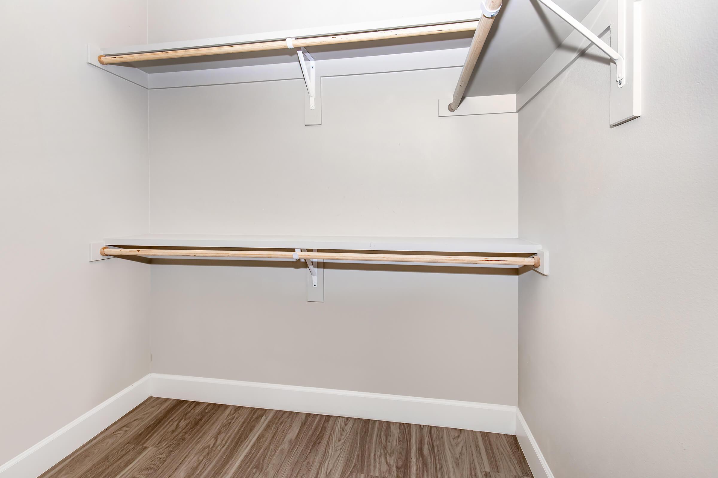 Empty closet interior featuring two wooden shelves and a clean, neutral wall. The floor is made of light brown laminate, and there are no items stored on the shelves. The space is well-lit and organized, giving a sense of openness.