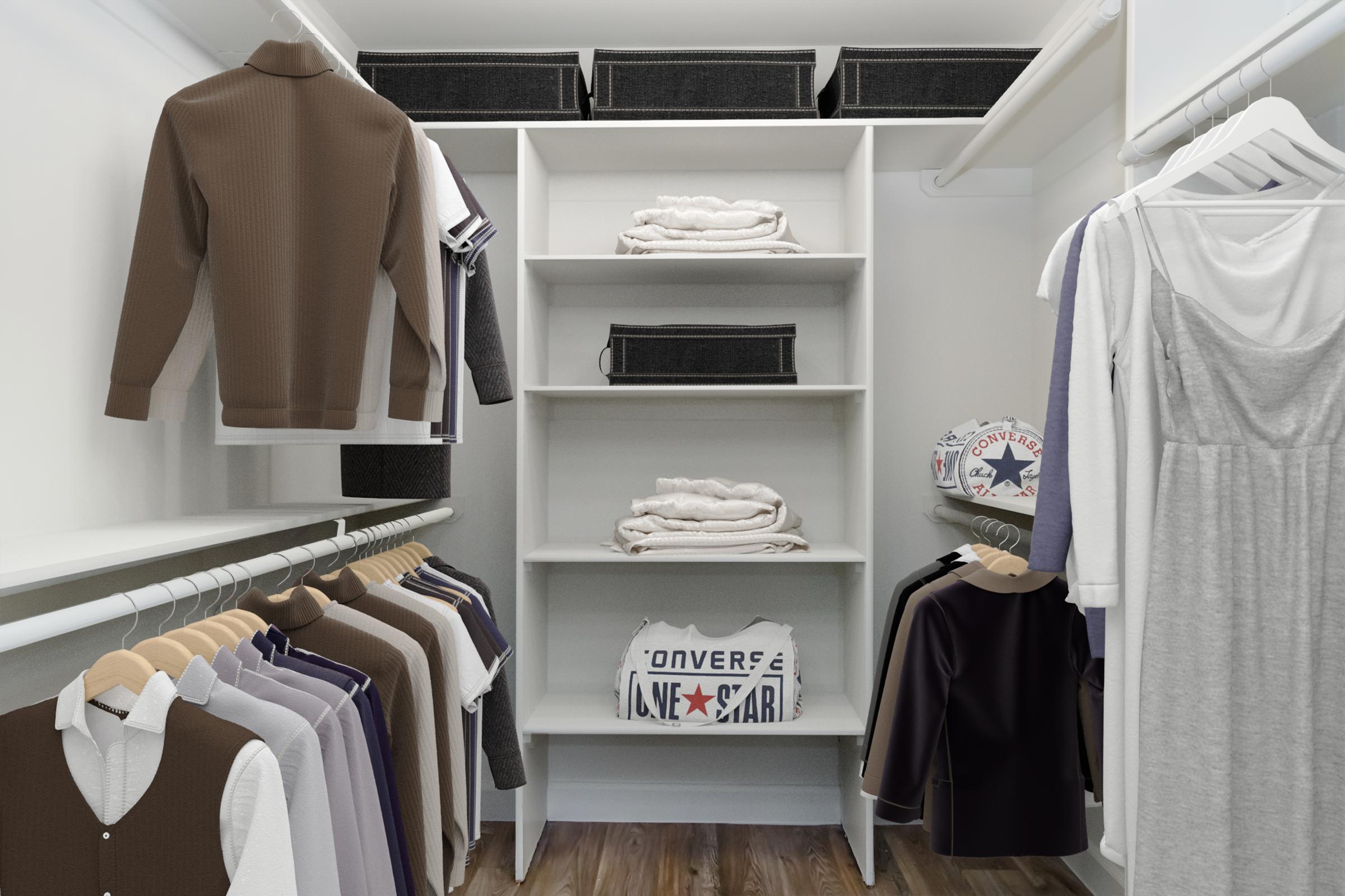 A well-organized closet featuring various clothing items, including shirts, jackets, and dresses hanging on hangers. Shelves display neatly folded towels and some storage boxes. The closet has a clean, modern aesthetic with a light color scheme and wooden flooring.