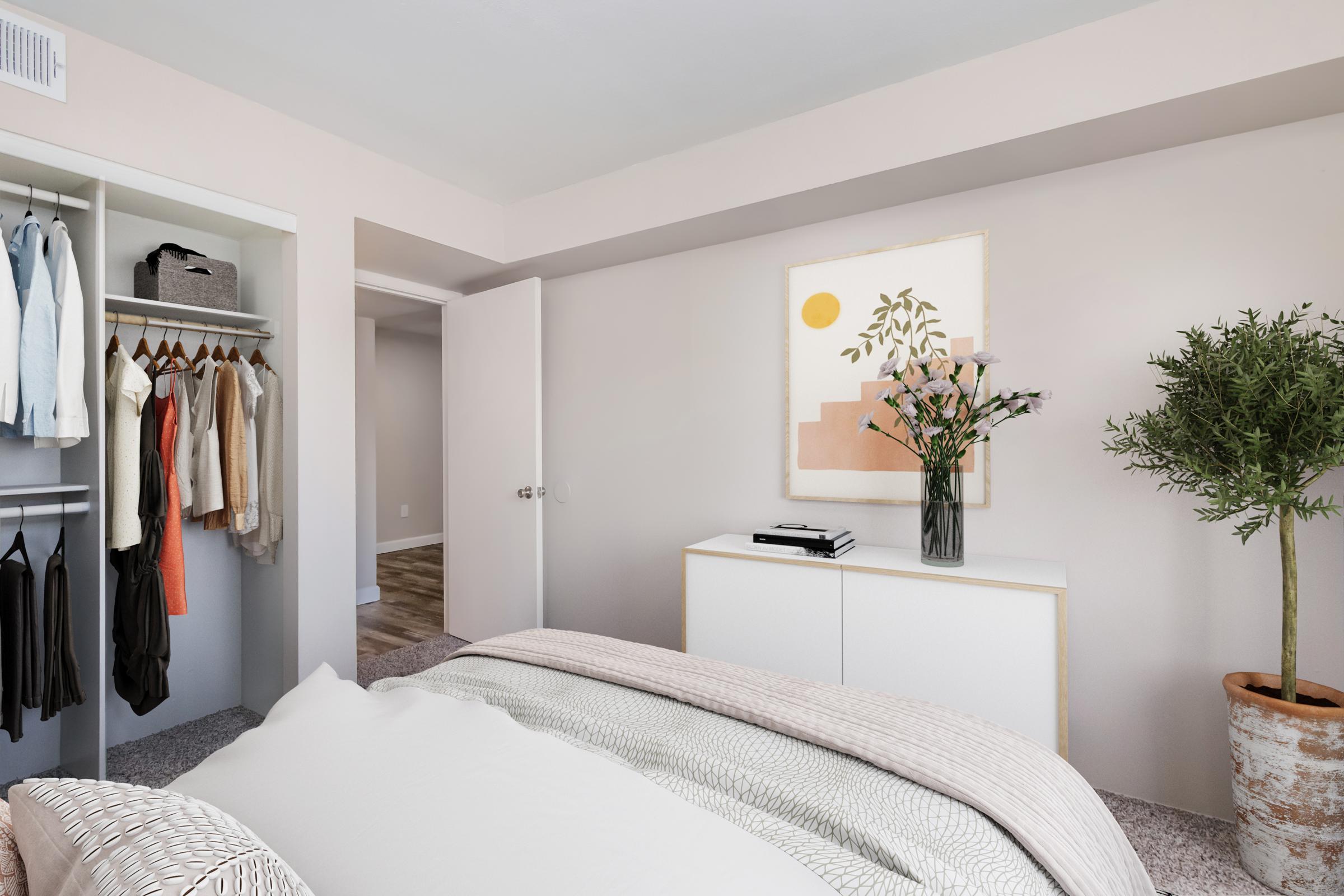 A cozy bedroom featuring a neatly made bed with a textured blanket, a white dresser, a vase of flowers, and a minimalist artwork on the wall. The closet is visible with hanging clothes, and there’s a potted plant in the corner, creating a calm and inviting atmosphere. Light walls enhance the spacious feel.