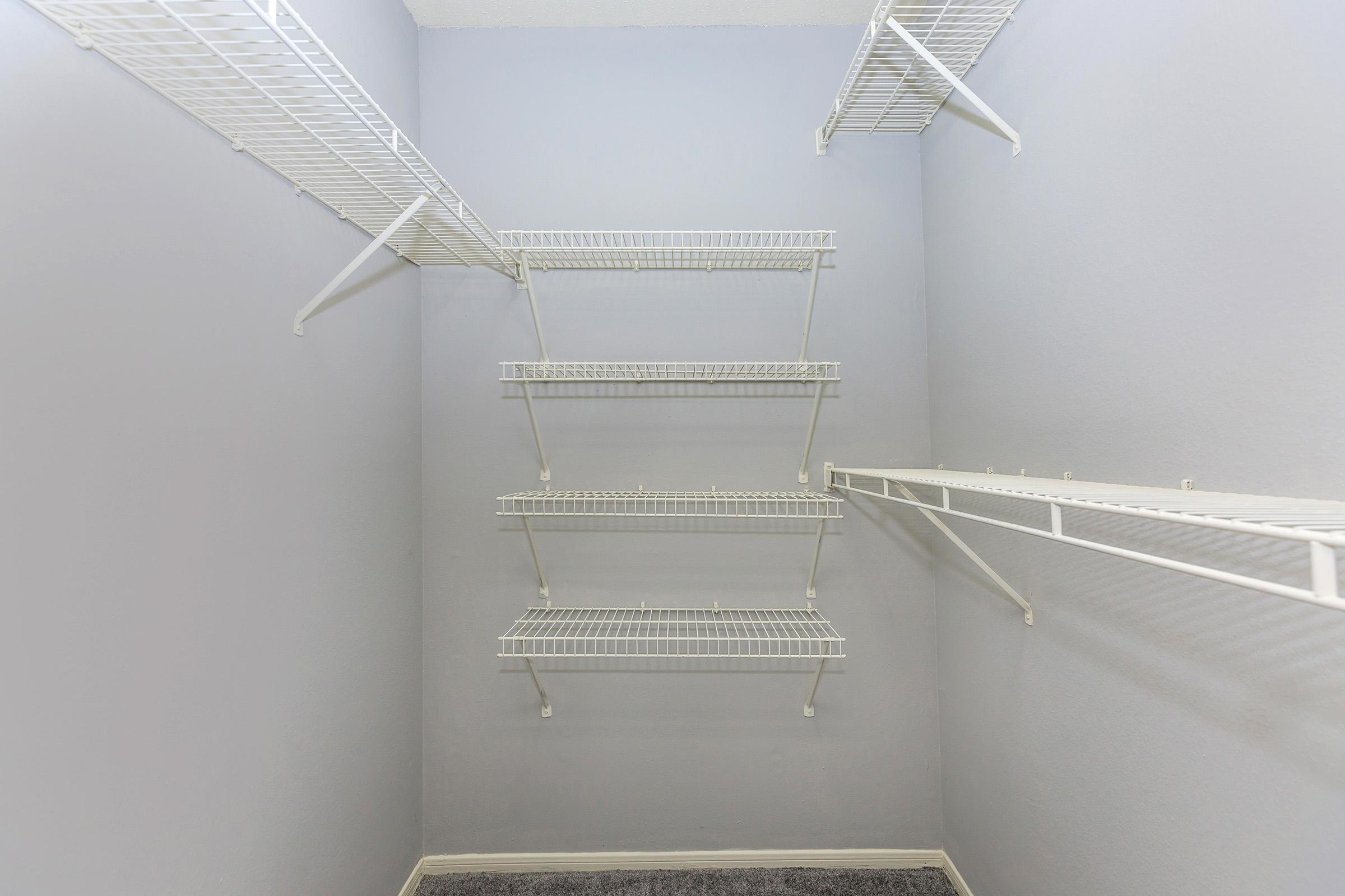 Empty closet with light gray walls and four wire shelving units mounted on the walls. The floor is carpeted, and there is a single wire shelf running along the top edge. The overall appearance is minimalistic and organized, suitable for storage.