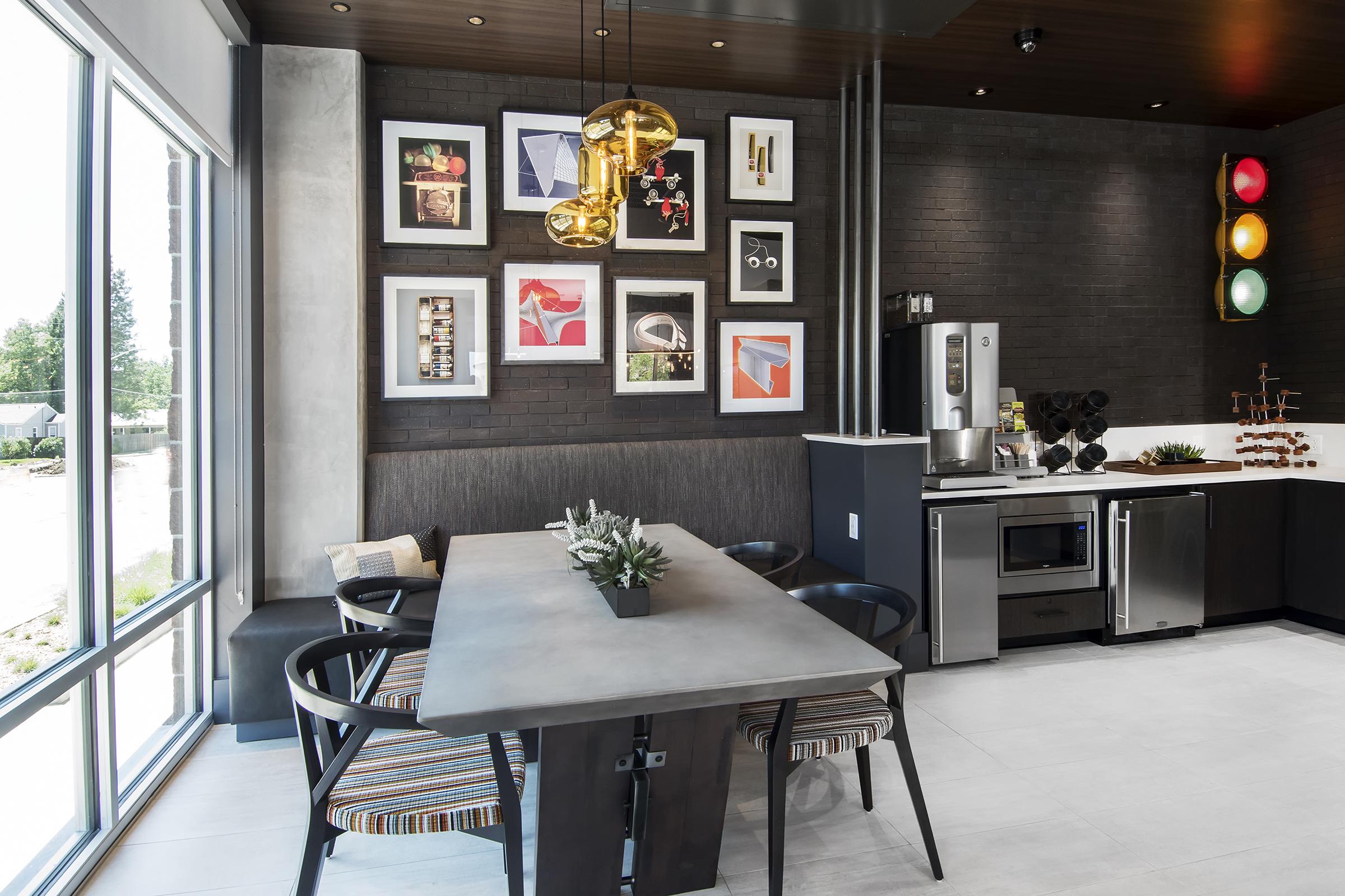 Modern kitchen interior featuring a sleek table with striped chairs, a wall adorned with framed artwork, and stylish pendant lighting. A stainless steel refrigerator and decorative plant are visible, along with a window that lets in natural light, enhancing the contemporary design.