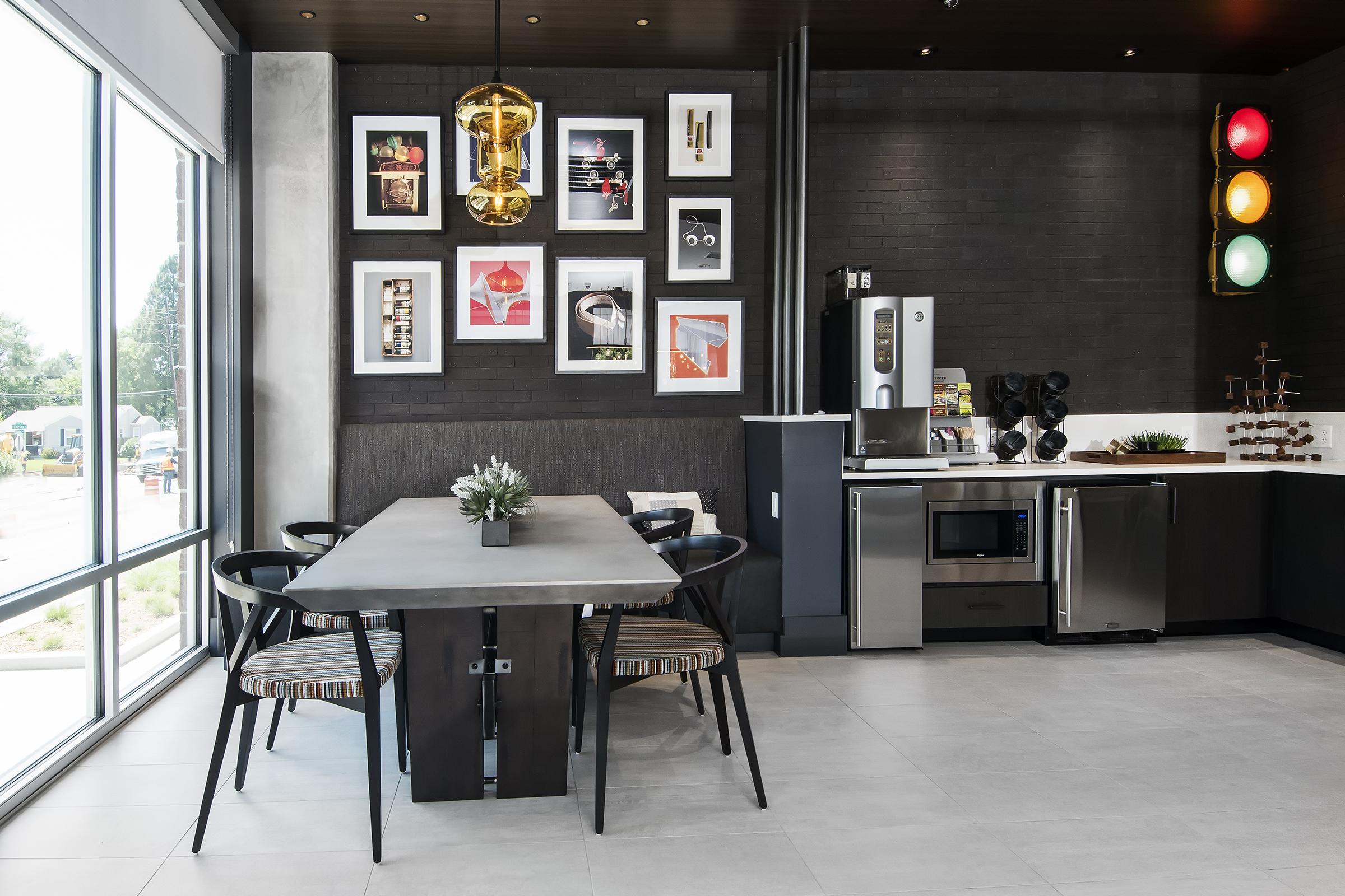 A modern kitchen featuring a sleek dining table with black chairs, an artistic wall adorned with framed prints, and contemporary appliances, including a refrigerator and microwave. Large windows allow natural light, highlighting the stylish decor and colorful traffic light display.