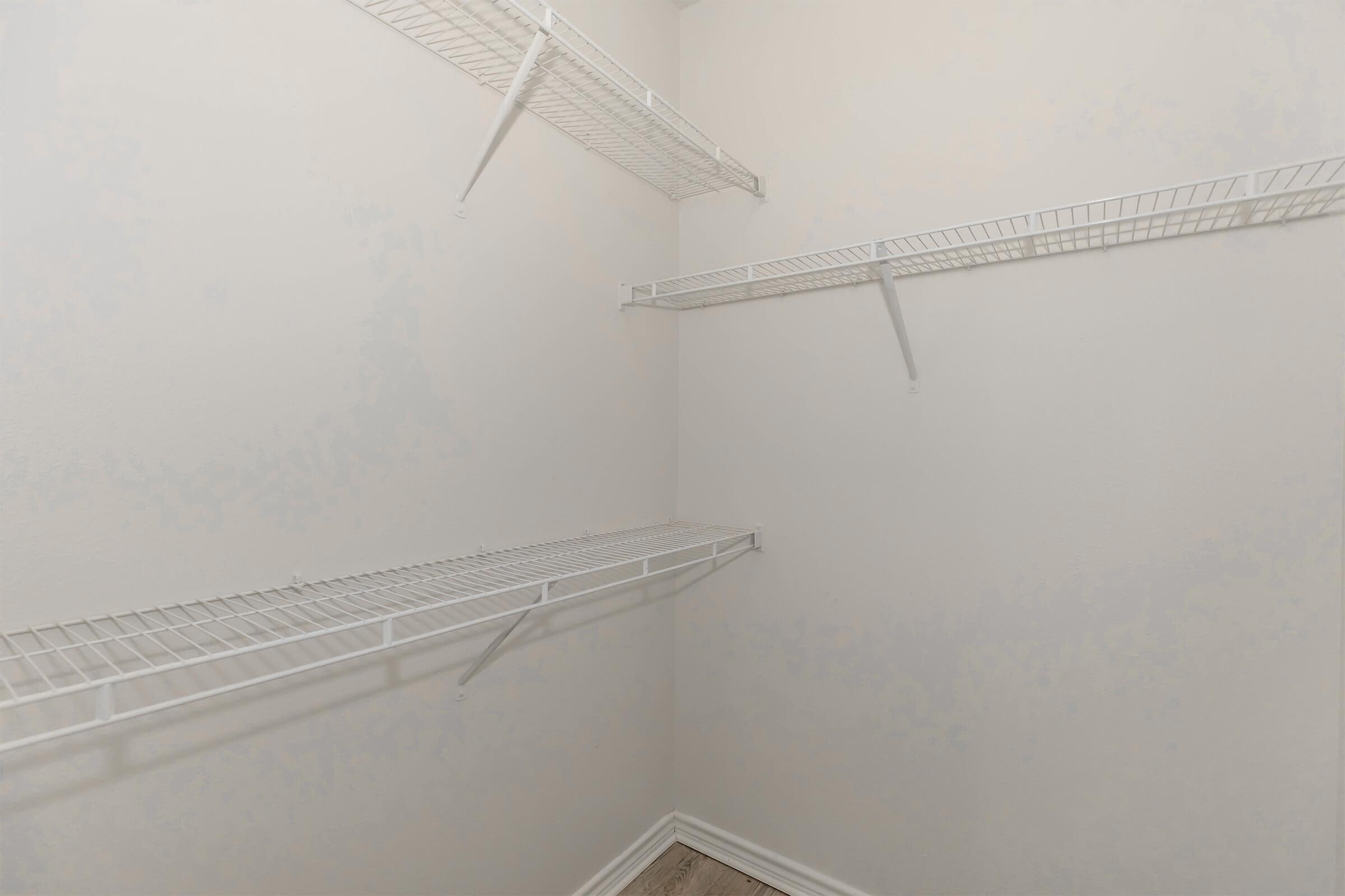 Empty closet with white wire shelving mounted on the walls. The walls are painted in a light color, and the floor appears to be a light-colored wood or laminate. There are no items or additional furniture in the space, creating a minimalistic and clean appearance.