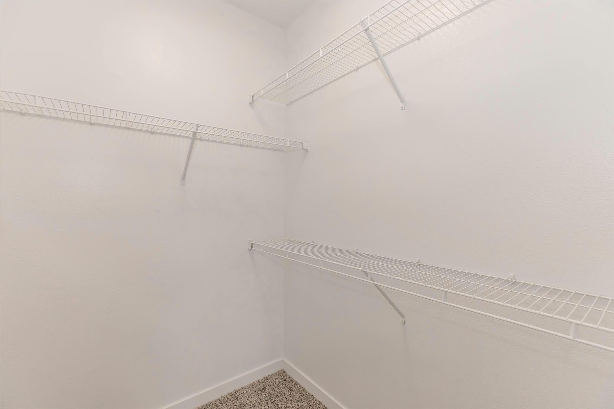 A clean, empty closet featuring white wire shelving against plain white walls and a beige carpeted floor, providing ample storage space and a minimalist aesthetic.