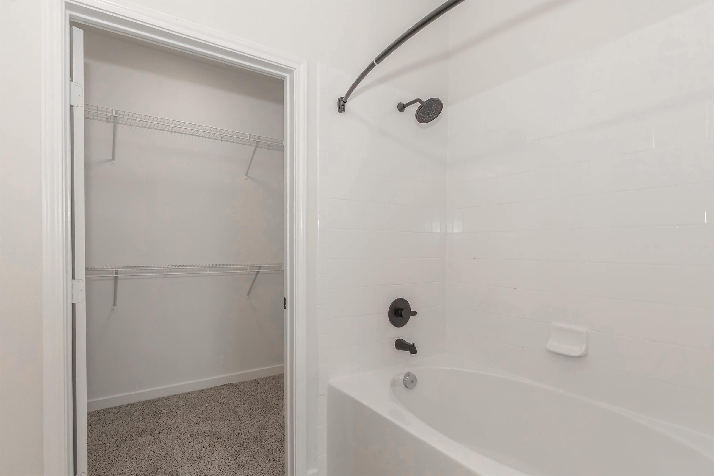 A clean bathroom featuring a shower-tub combination, a sleek black showerhead, and a bathtub faucet. Adjacent to the bathroom is a walk-in closet with wire shelving and carpeted flooring, creating a spacious and organized area. The walls are painted a light color, enhancing the bright atmosphere.