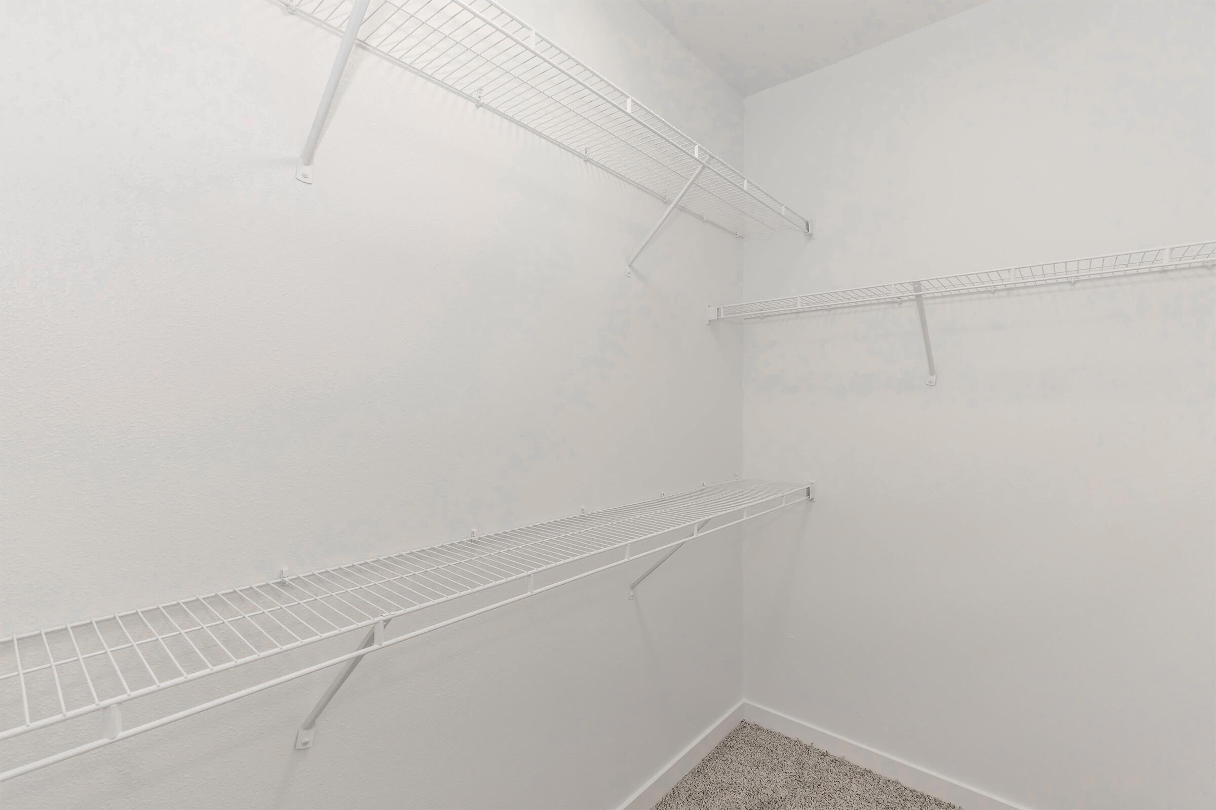 A clean, empty closet featuring white wire shelving attached to the walls. The walls are painted light, and the floor is covered with carpet. The space is well-lit and organized, showcasing the potential for storage or organization.