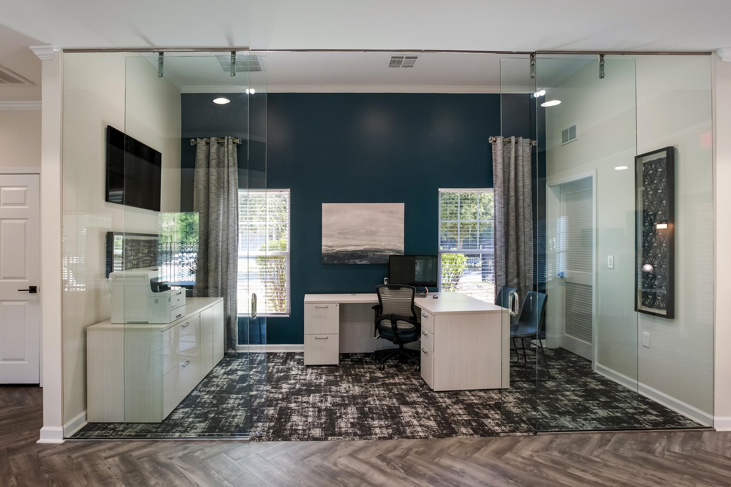 A modern lobby with comfortable seating, including patterned and solid color sofas, a decorative rug, and large windows providing natural light. There's a reception desk in the background, adorned with blue accents, and plants adding a fresh touch to the inviting space.