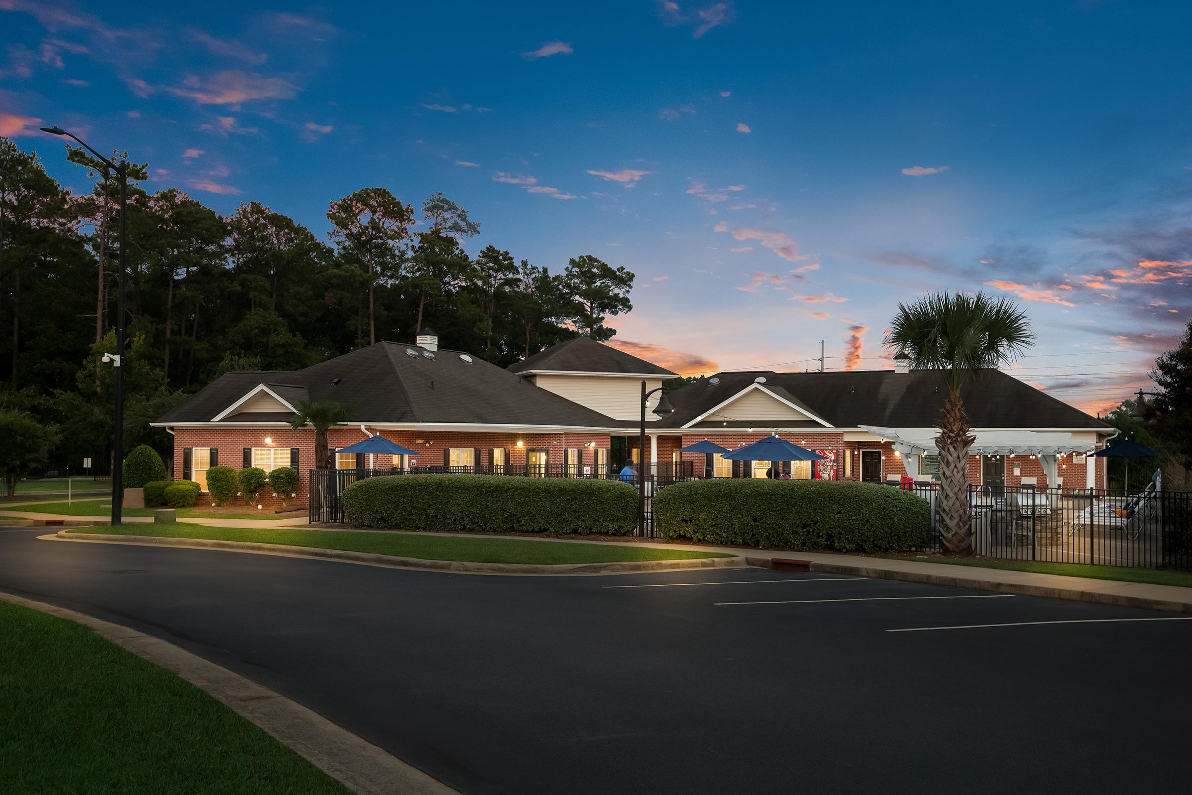 Sign for Ardmore Pointe Apartment Homes, featuring the name prominently displayed on a brick structure with landscaping, illuminated by garden lights. The background shows a peaceful evening sky.