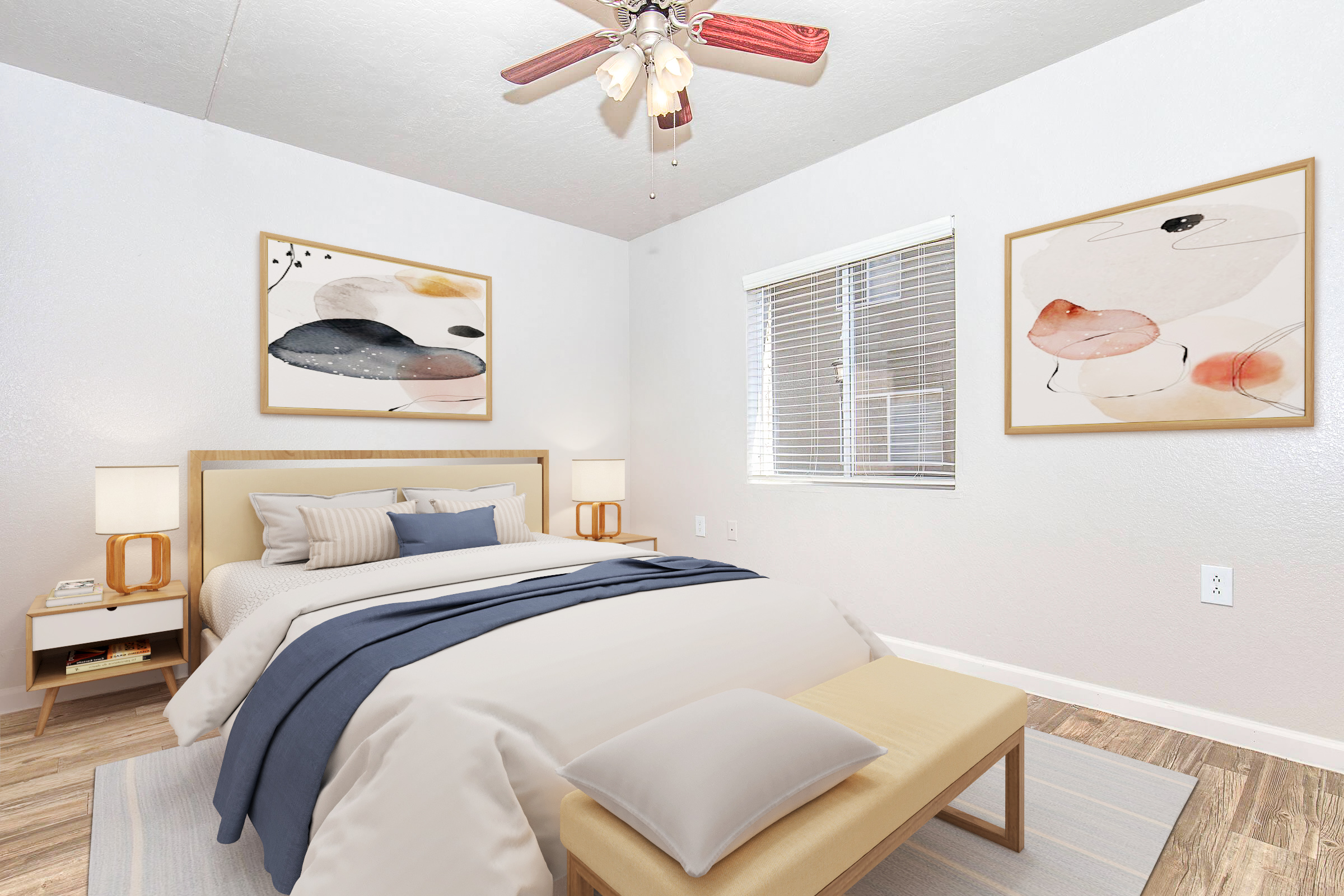 A cozy bedroom featuring a comfortable bed with a light gray duvet and decorative pillows. There are two framed wall artworks, a wooden nightstand with lamps, and a bench at the foot of the bed. A ceiling fan provides cooling, and a window allows natural light to enter, highlighting the modern decor.