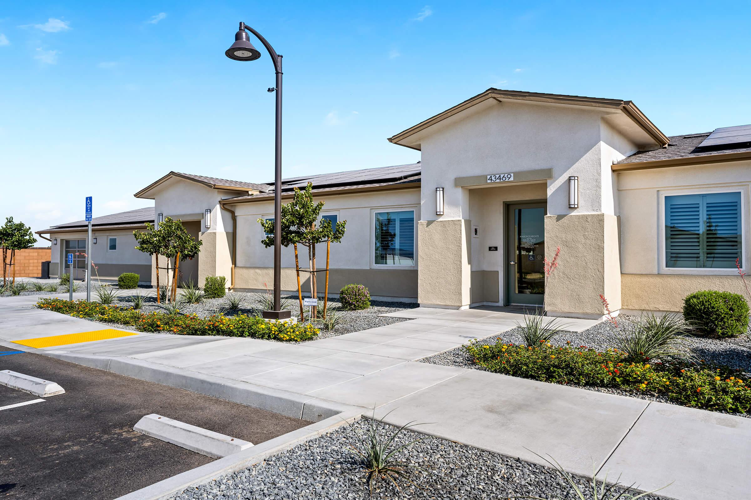 A single-story building with a light-colored exterior and a welcoming entrance. Has a neatly landscaped areas with small trees and plants.
