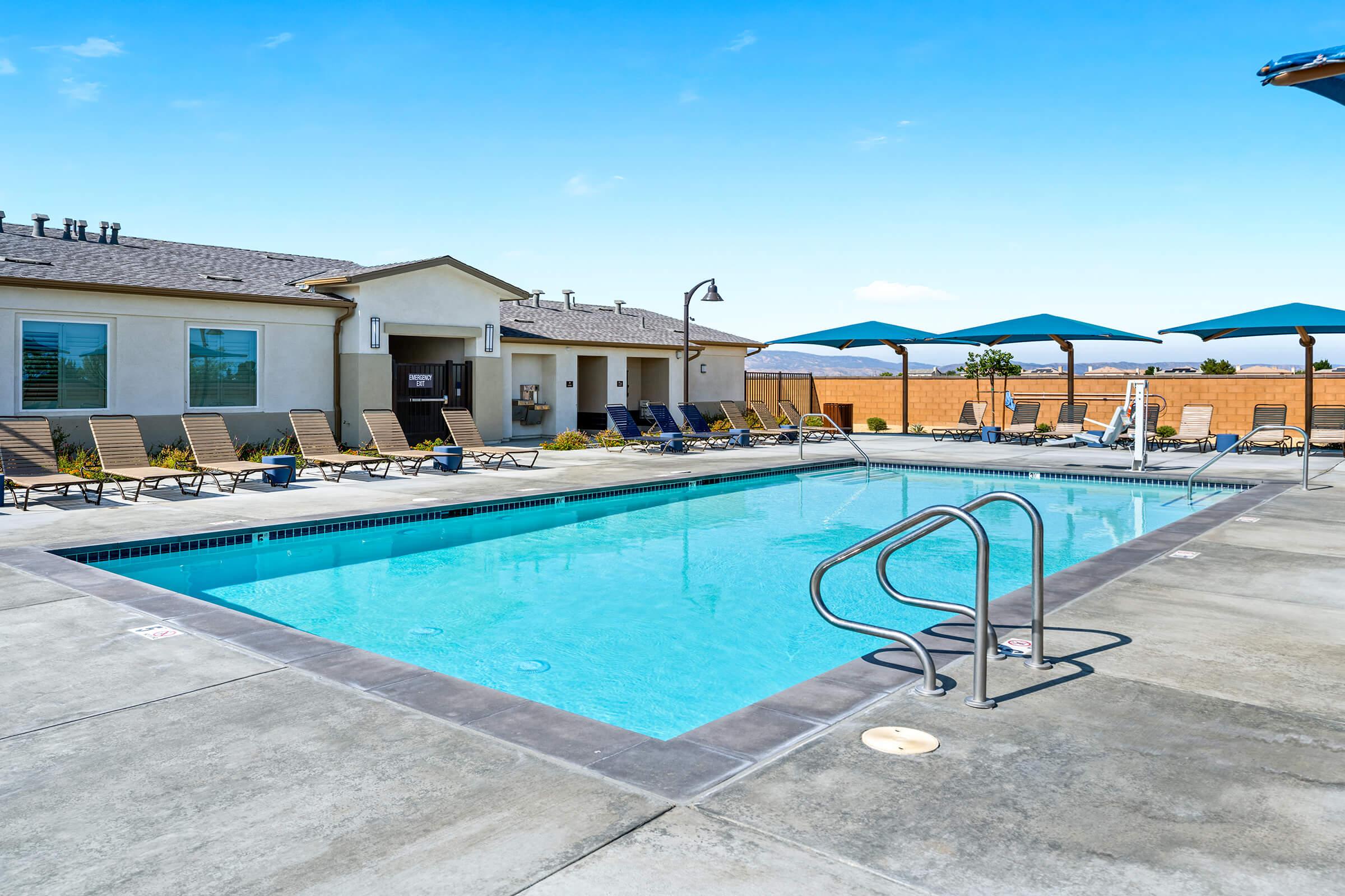 An inviting swimming pool surrounded by lounge chairs and blue umbrellas. A bright blue sky with minimal clouds above.