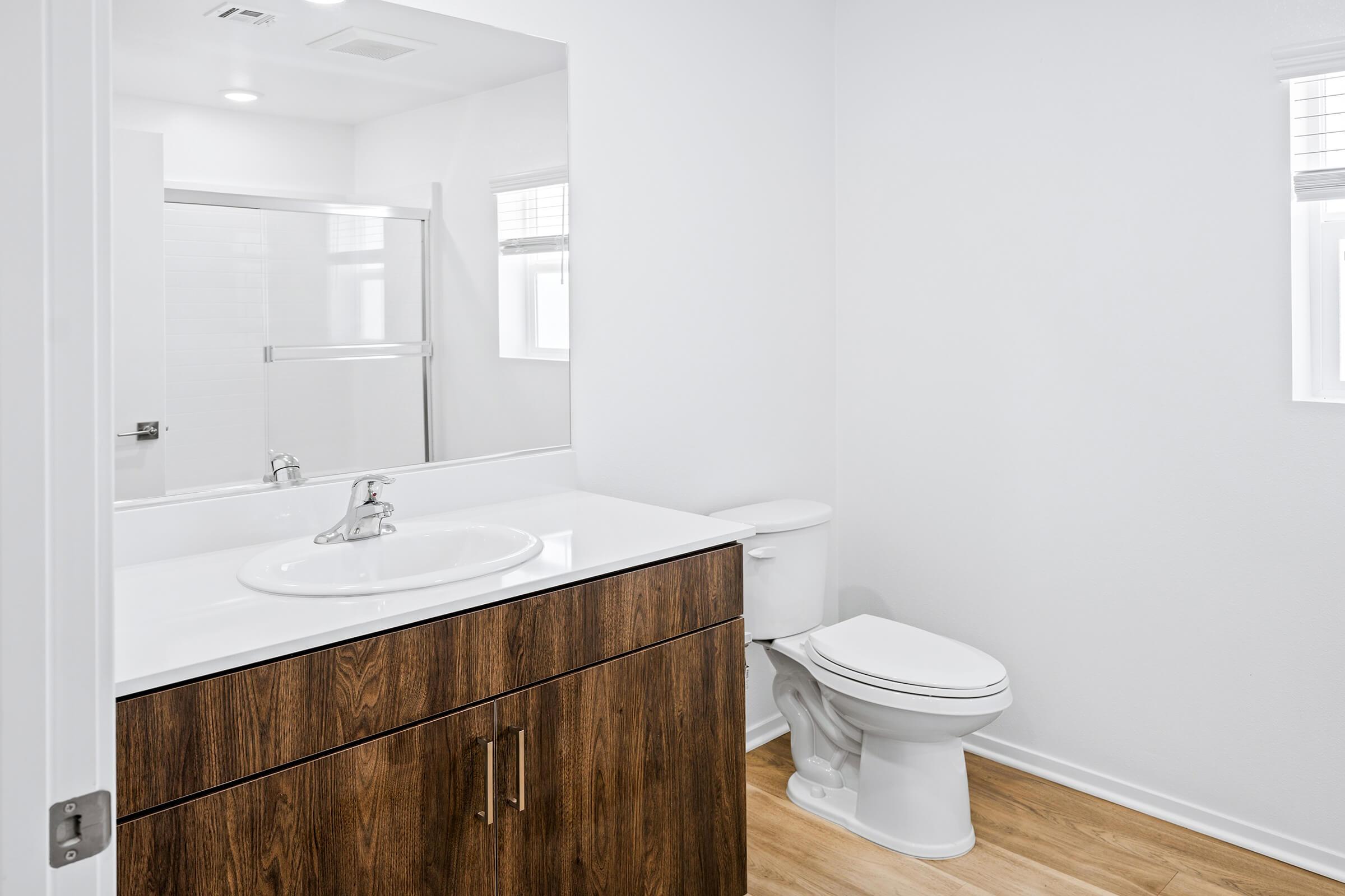 A bathroom with a white sink, a wooden vanity with drawers, a white toilet, and a glass-enclosed shower. 