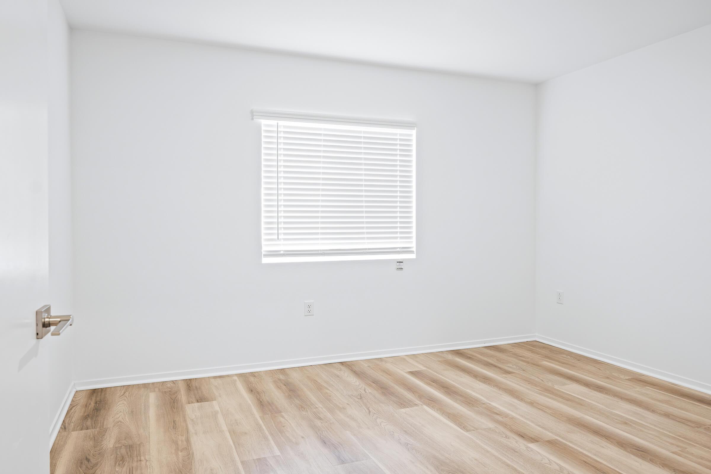 An empty room with light-colored walls and hardwood flooring. 