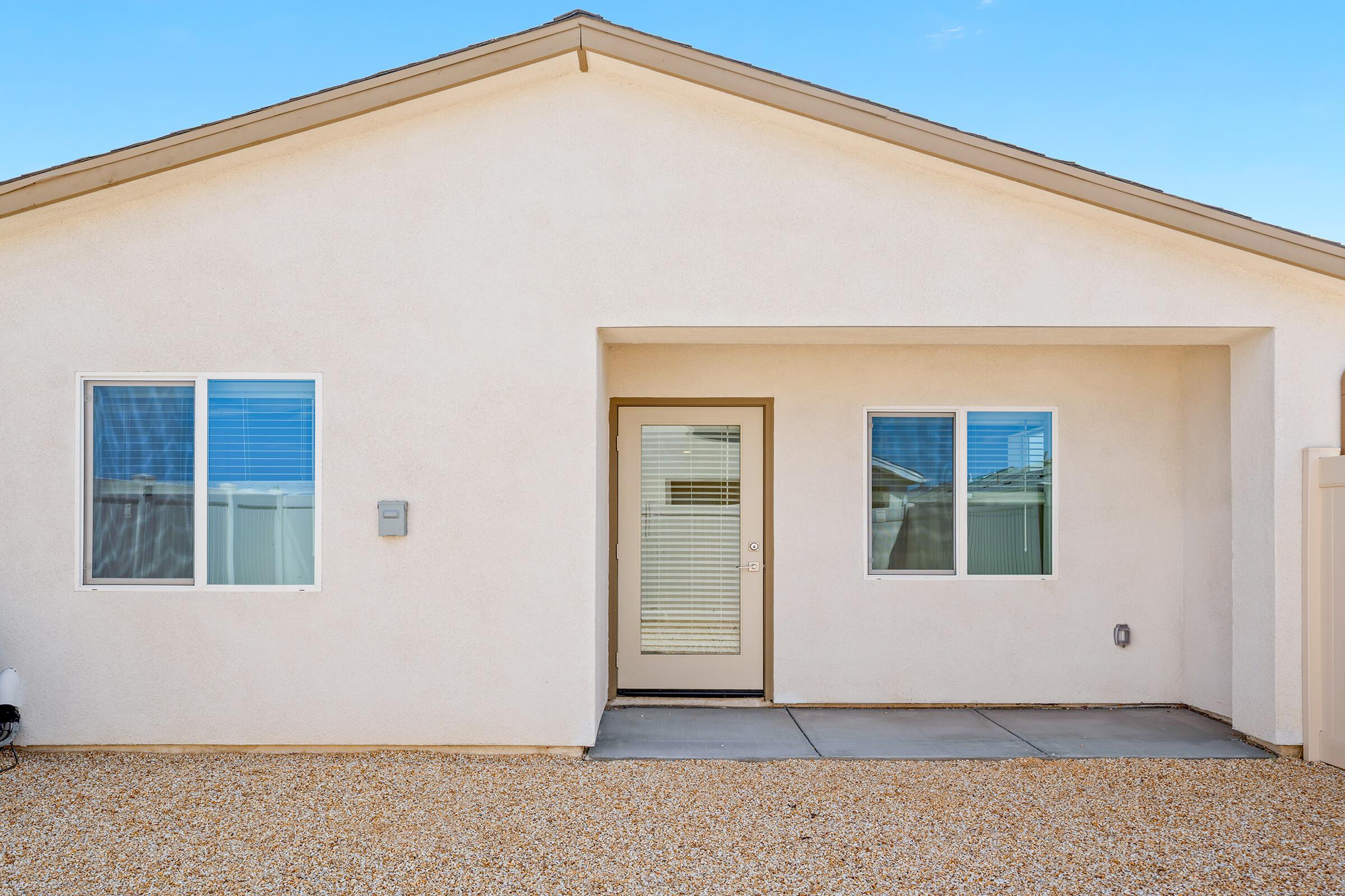 A single-story home with light beige exterior. The area in front has light gravel, and the setting is clear and sunny.