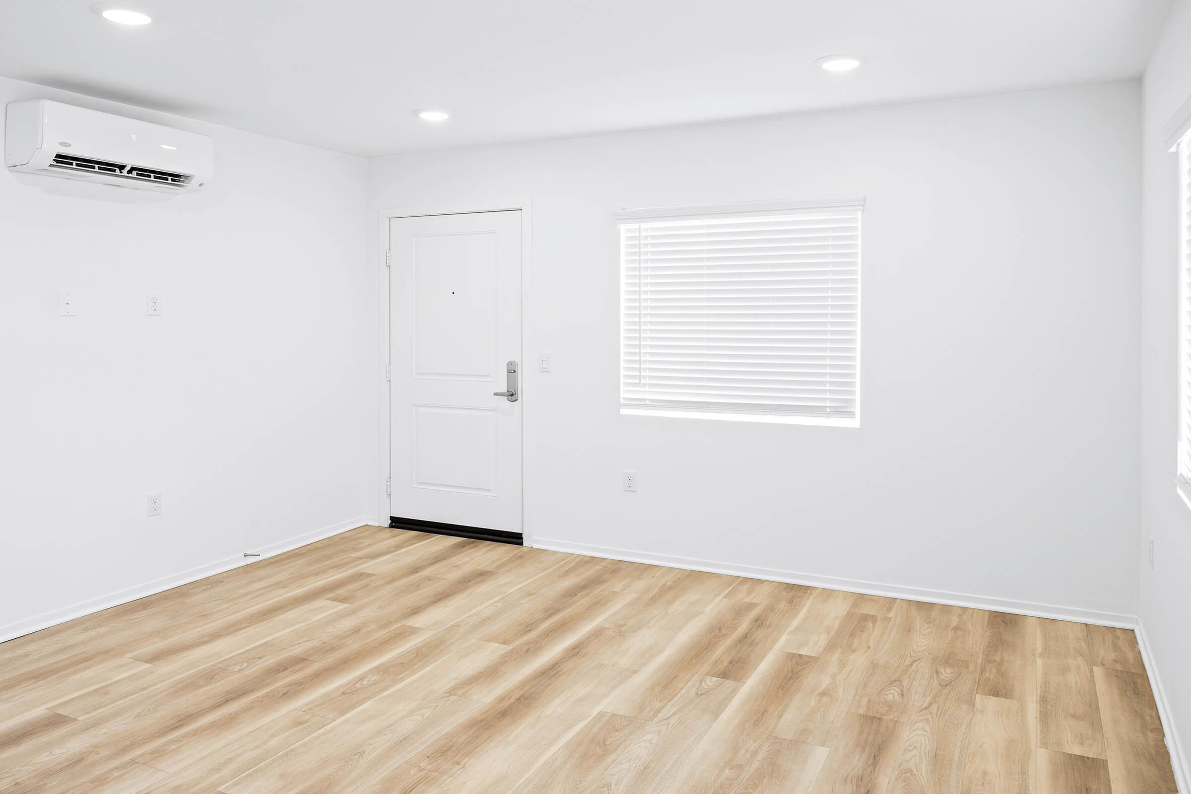 An empty room with light-colored walls and hardwood flooring. 