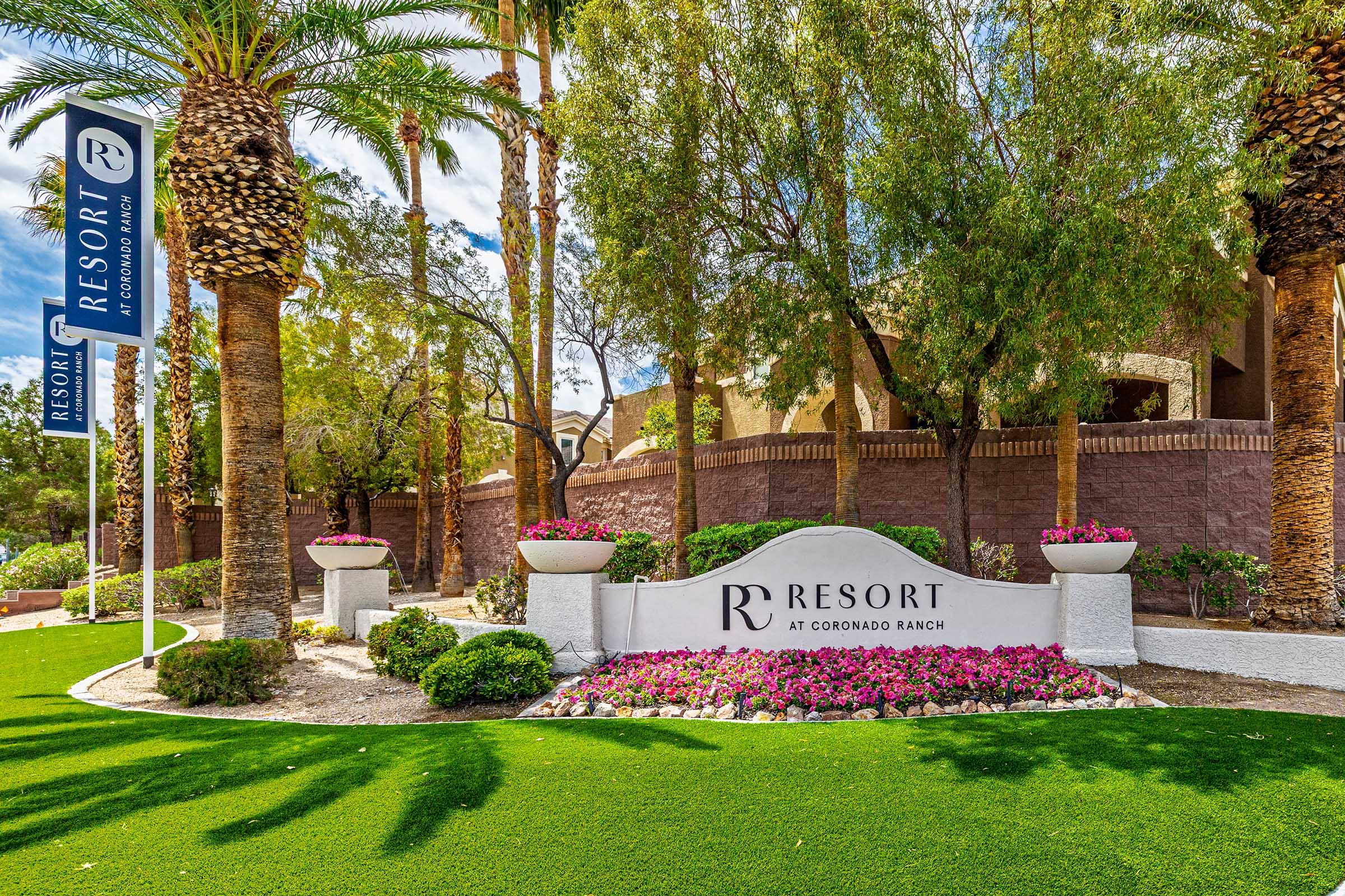 Sign for "Resort at Coronado Ranch" surrounded by lush green grass, vibrant pink flowers, and palm trees. The sign features a modern design with the resort's name prominently displayed. The scene conveys a welcoming and tranquil atmosphere typical of a resort setting.