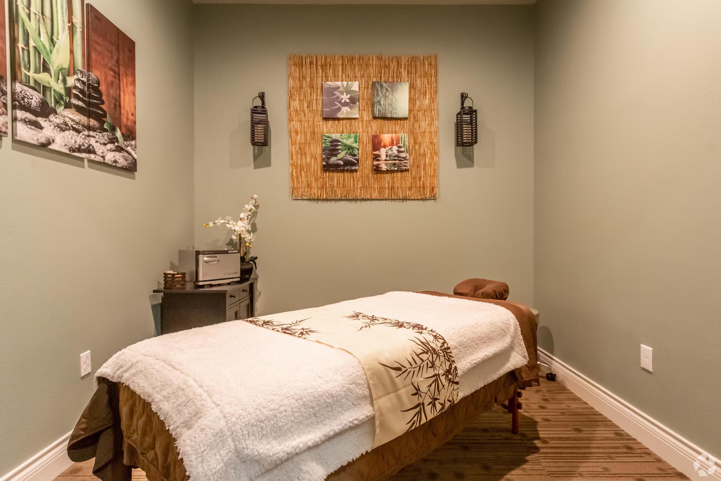 A serene massage therapy room featuring a massage table covered with a plush blanket. The walls are painted a soothing green, adorned with nature-themed artwork and bamboo accents. Soft lighting from wall sconces creates a relaxing ambiance, enhancing the tranquil atmosphere for clients.