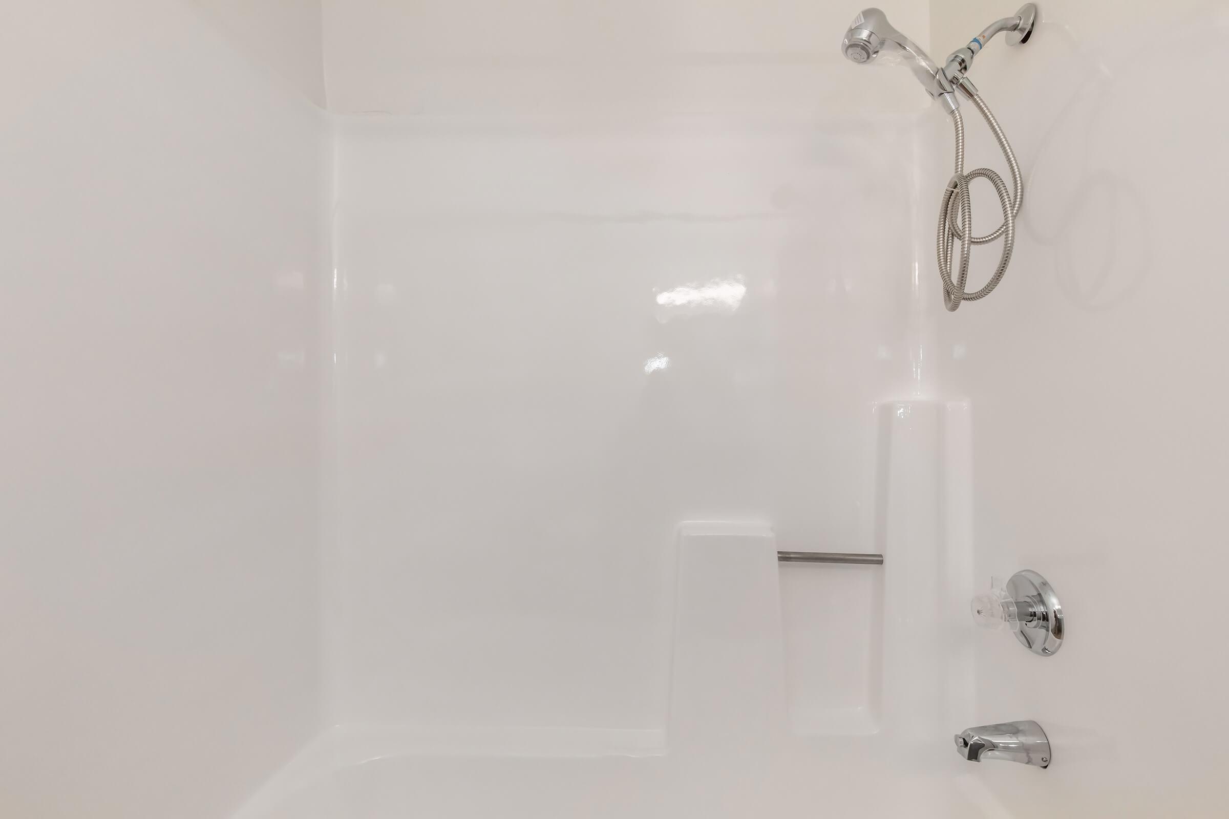 A clean, modern shower stall featuring a smooth white wall, a handheld showerhead, and grab bars for safety. The design includes a built-in seat for convenience, with a minimalistic aesthetic ideal for a contemporary bathroom.