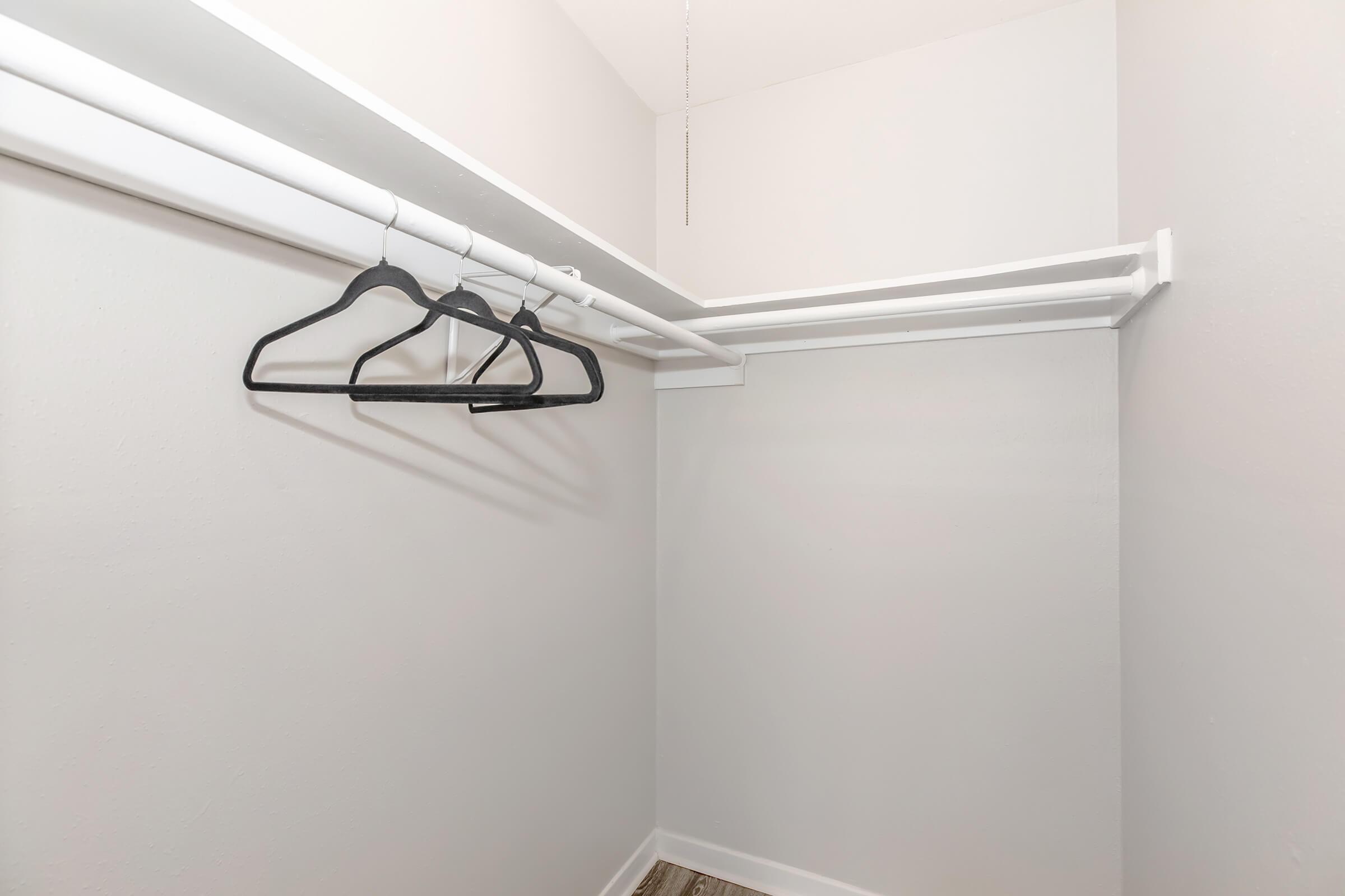 Empty closet with white walls and two rows of white hanging rods. Three black hangers are suspended from the top rod, and the floor is visible with a light-colored surface. The closet appears clean and minimalistic, with no additional items or decorations.