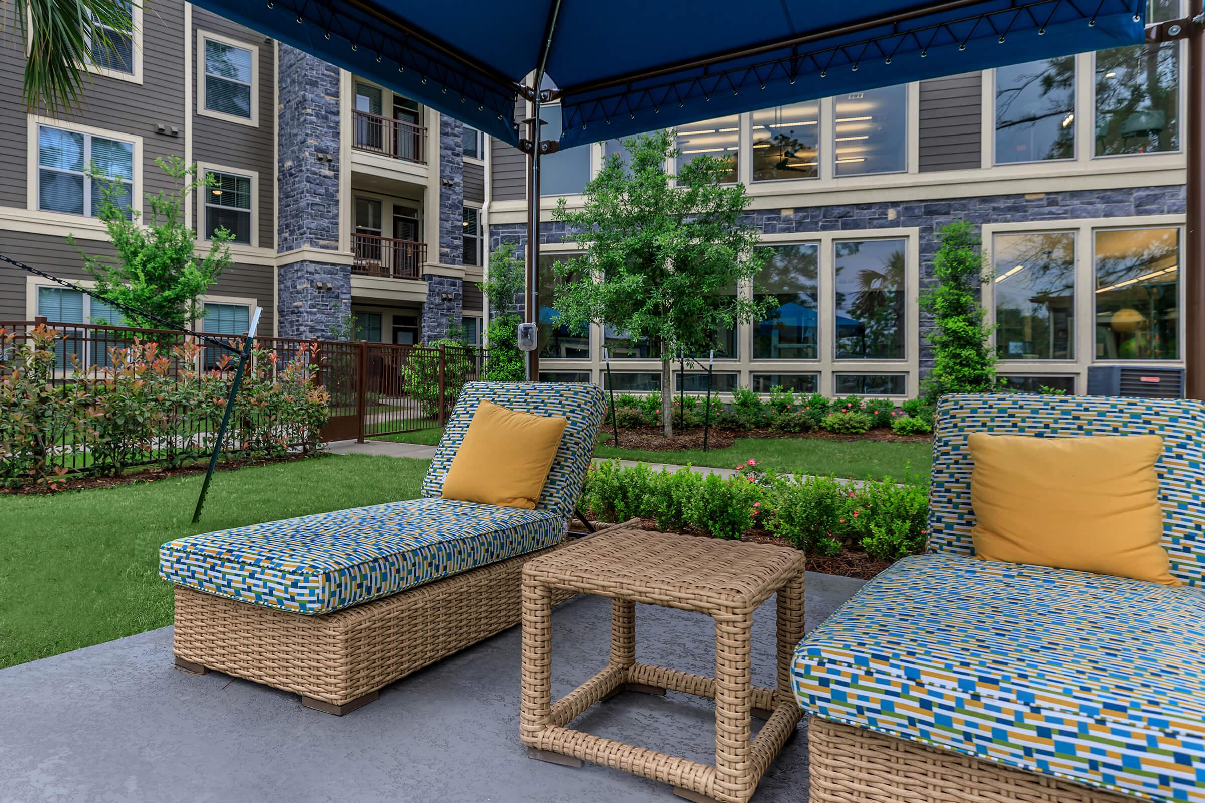 Cabana seating area with two padded loungers and green landscaping backdrop.