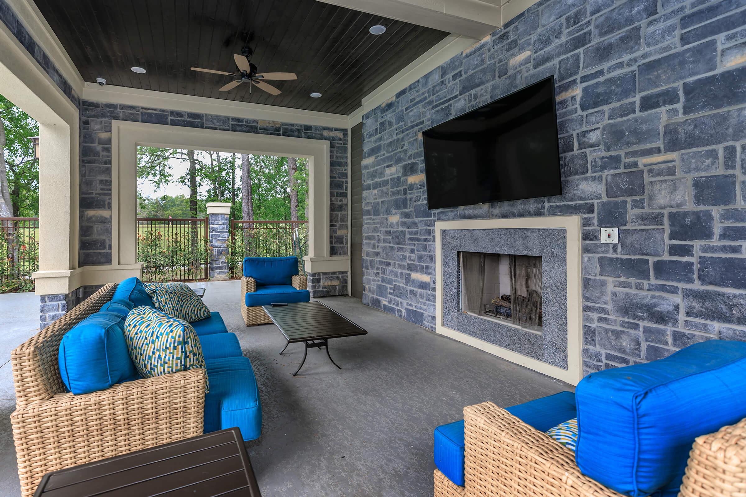 Outdoor lounge with fireplace, tv, and plush blue cushions on wicker seating.