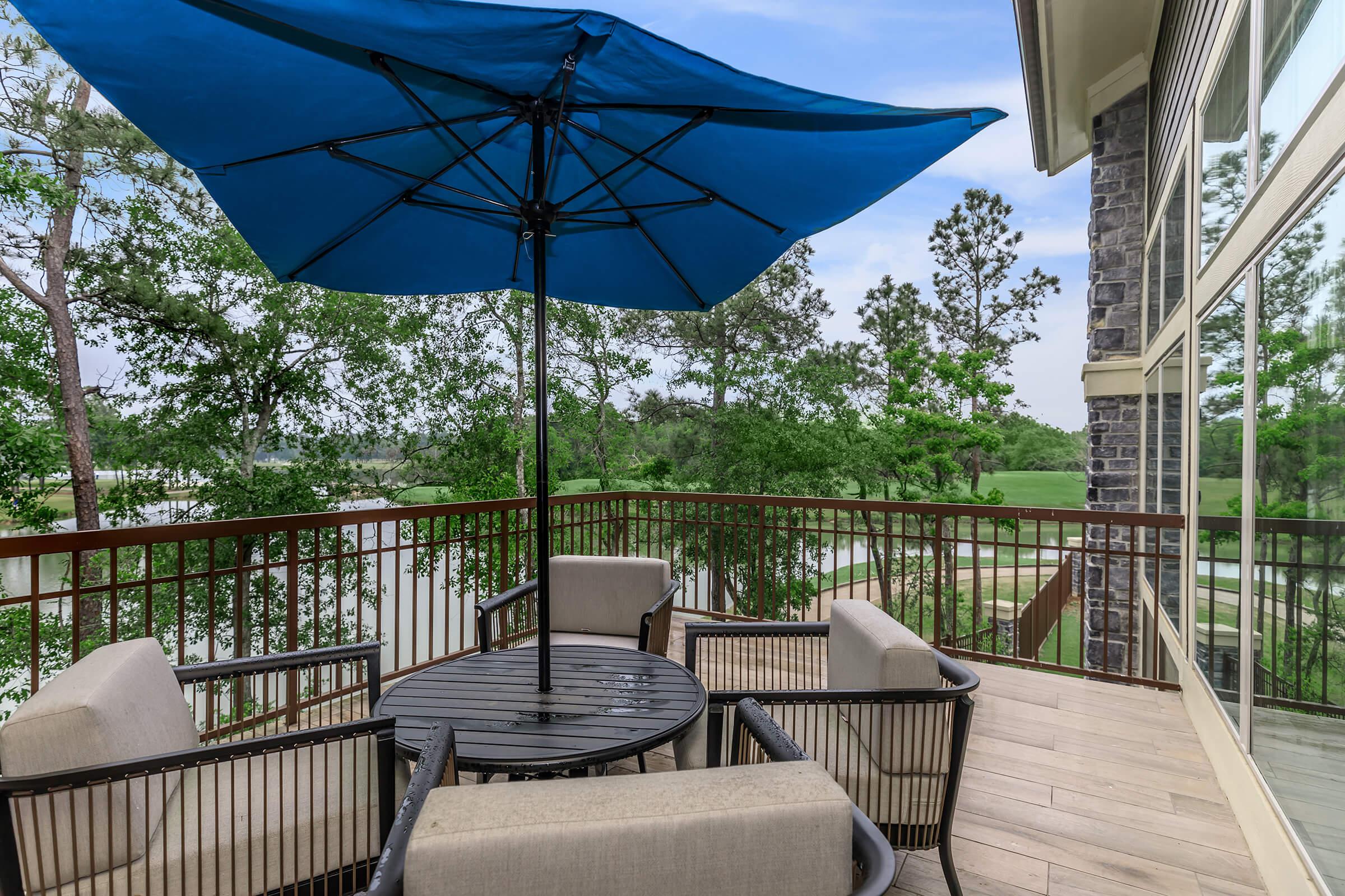 Seating area on deck with patio furniture and blue umbrella. View of landscaping.
