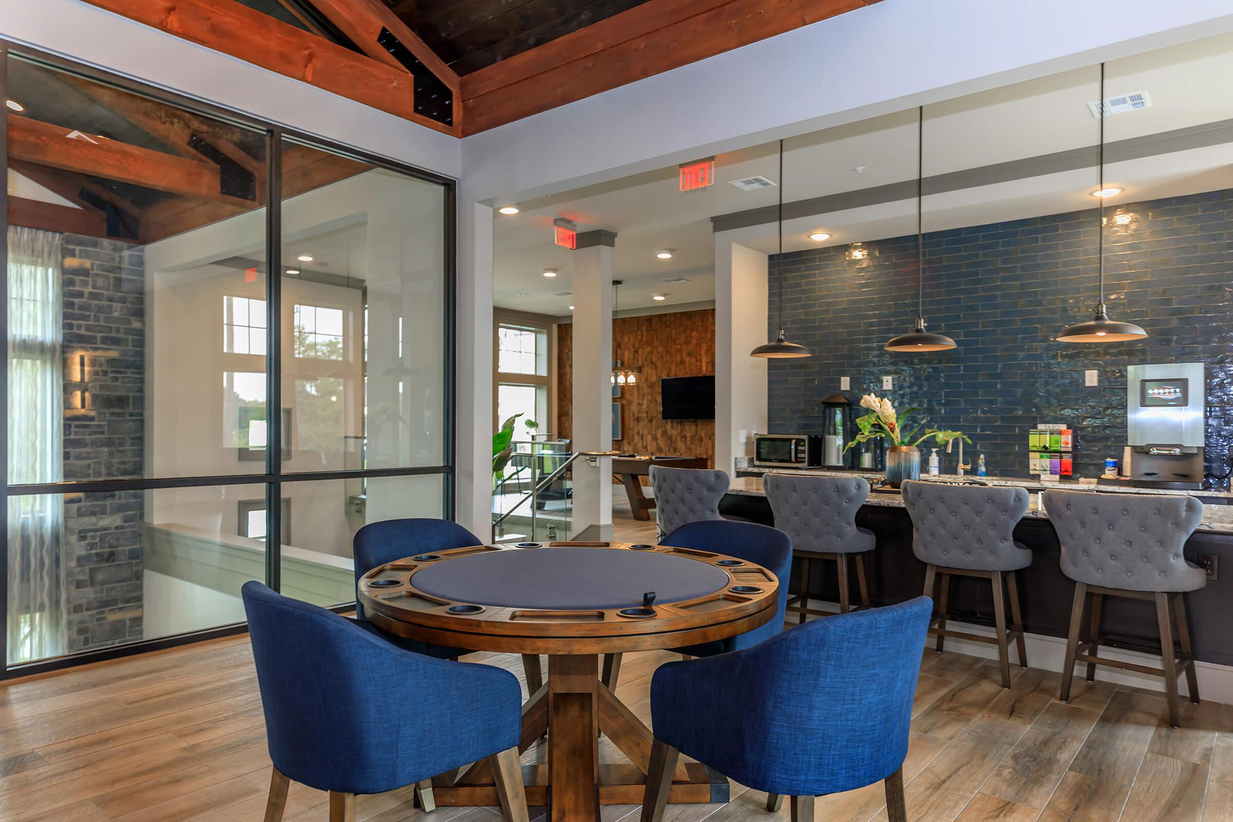 Luxury resident lounge. Table and chairs, chairs at kitchen counter behind, picture window to left.