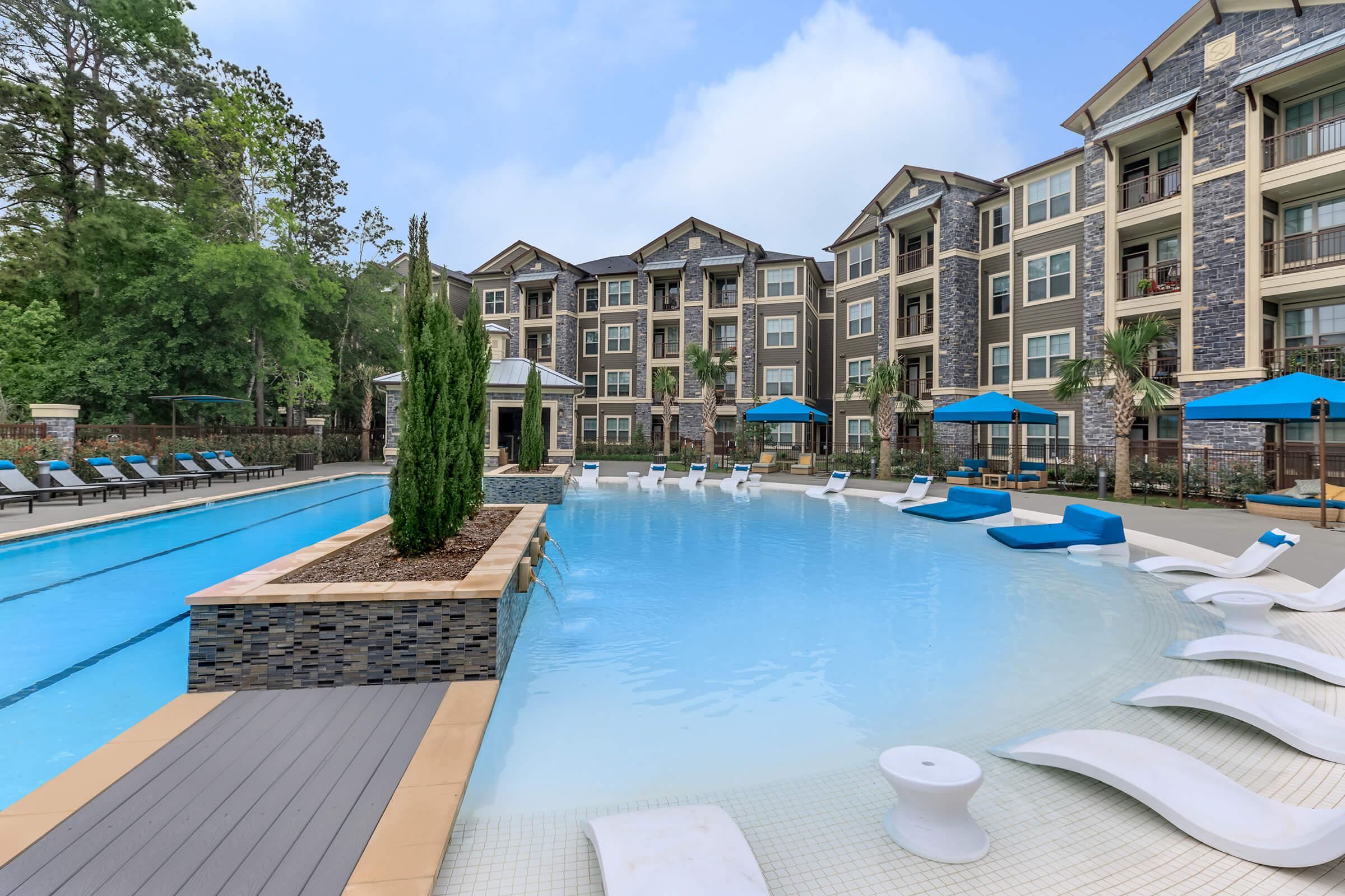 Resort-style pool with beach entry, water loungers, and apartment building to the right.