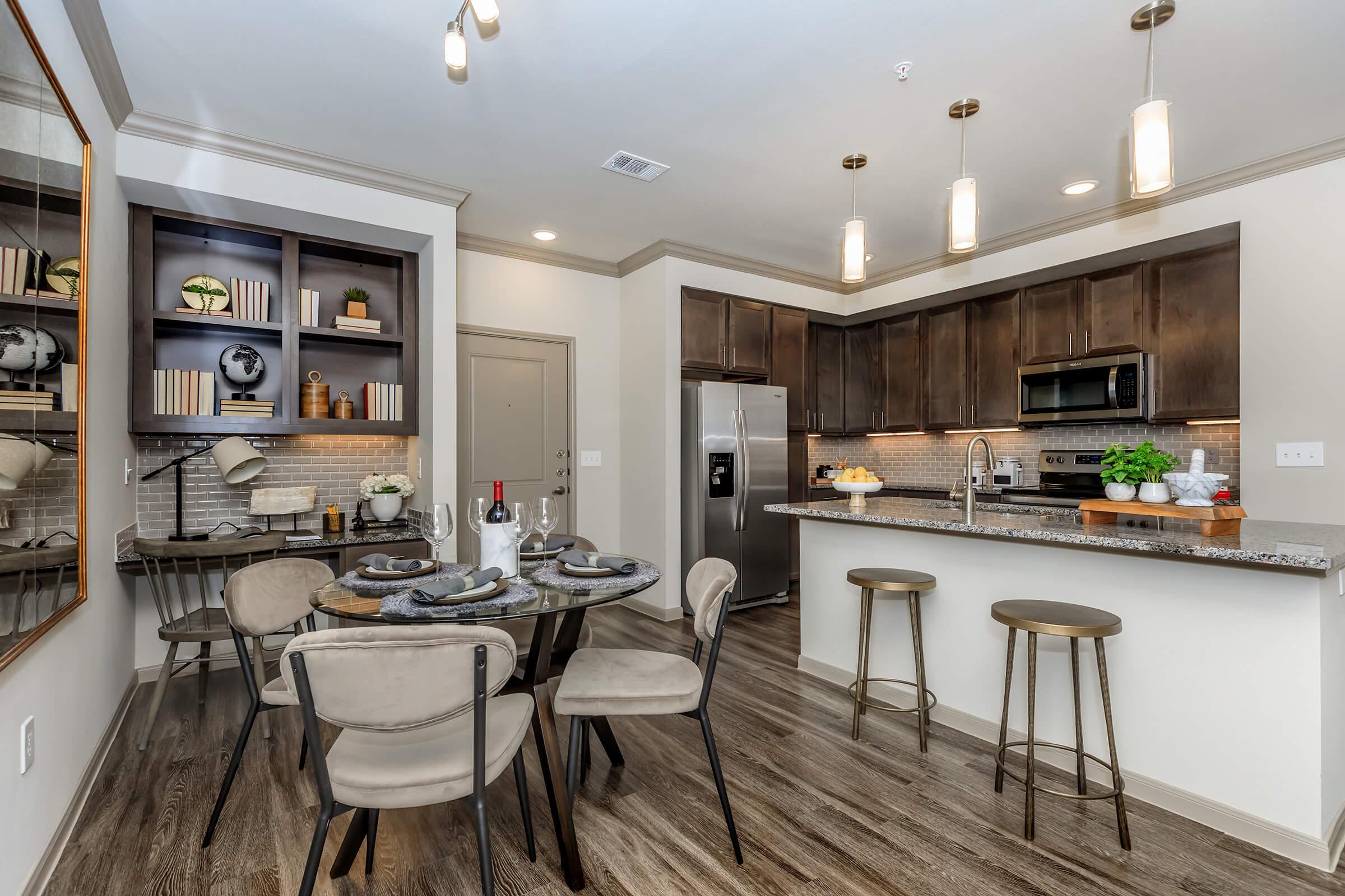 Dining area with built in shelving and desk area on left. Kitchen island with barstools on right.