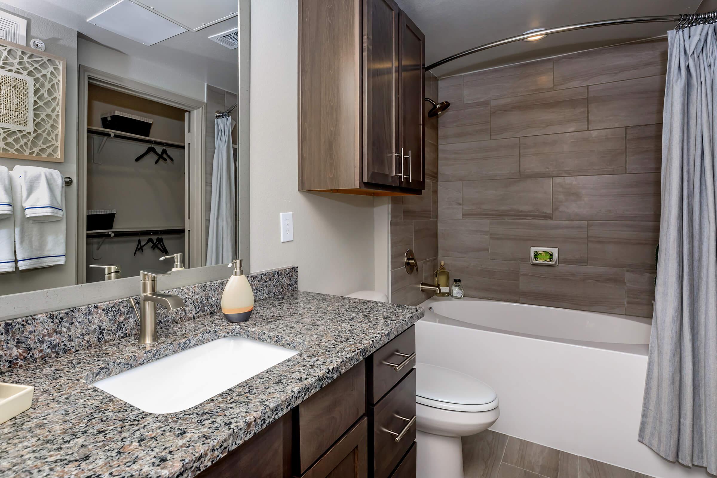 Modern bathroom in brand new apartment. Granite counters, tub with surround, and large mirror.