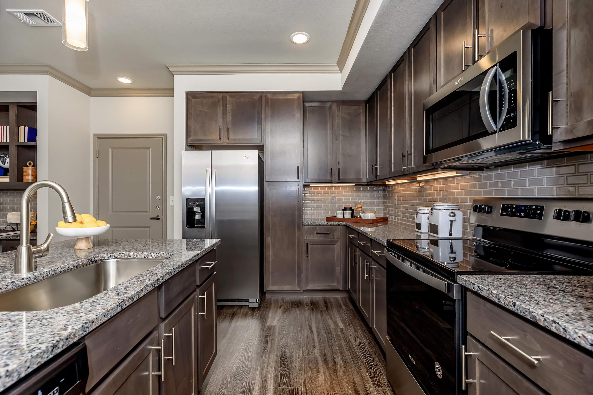 Modern kitchen with granite countertops, rich cabinets, and stainless steel appliances.