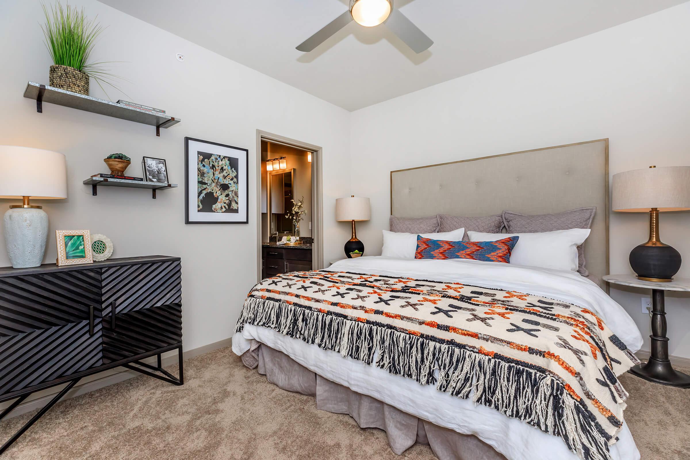 Spacious bedroom with staged furniture. Carpet flooring and ceiling fan.