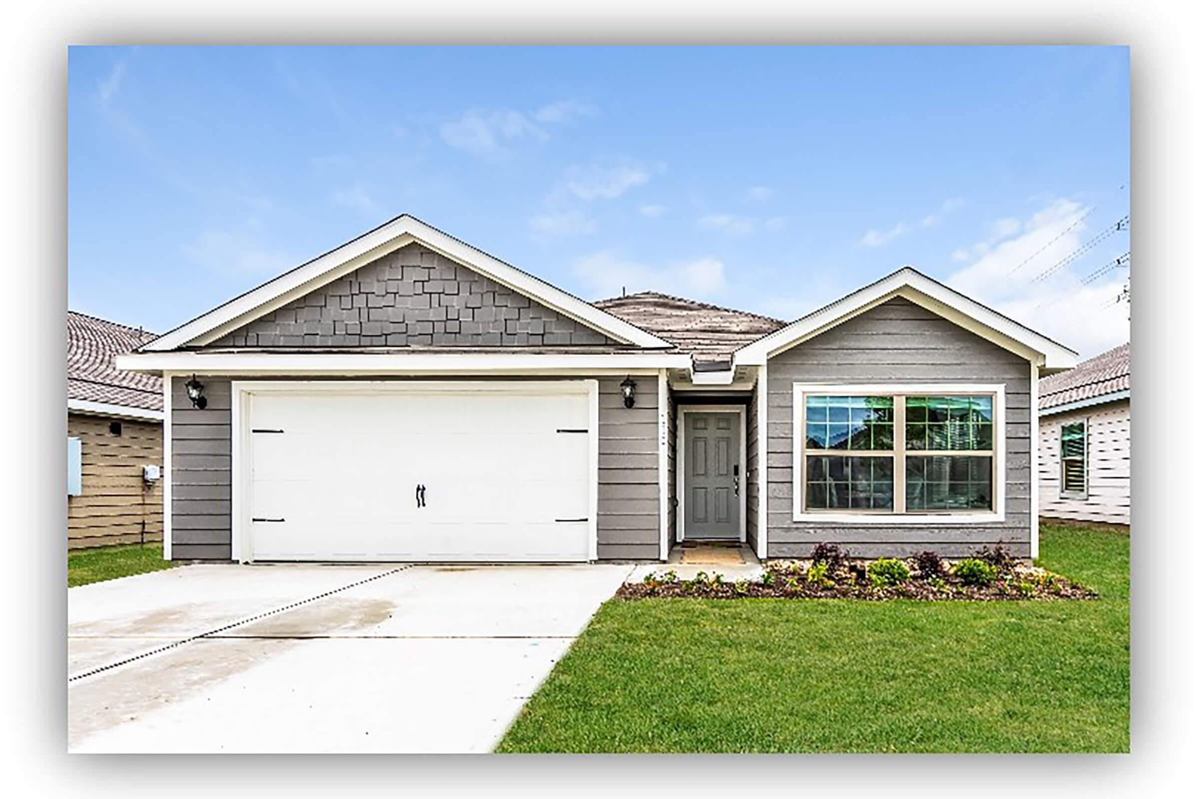 A modern single-story house with gray siding, a two-car garage, and a well-maintained lawn. The front features a symmetrical design with a large window on the left and a smaller one on the right. The driveway is concrete, and the sky is clear and blue, enhancing the curb appeal of the home.