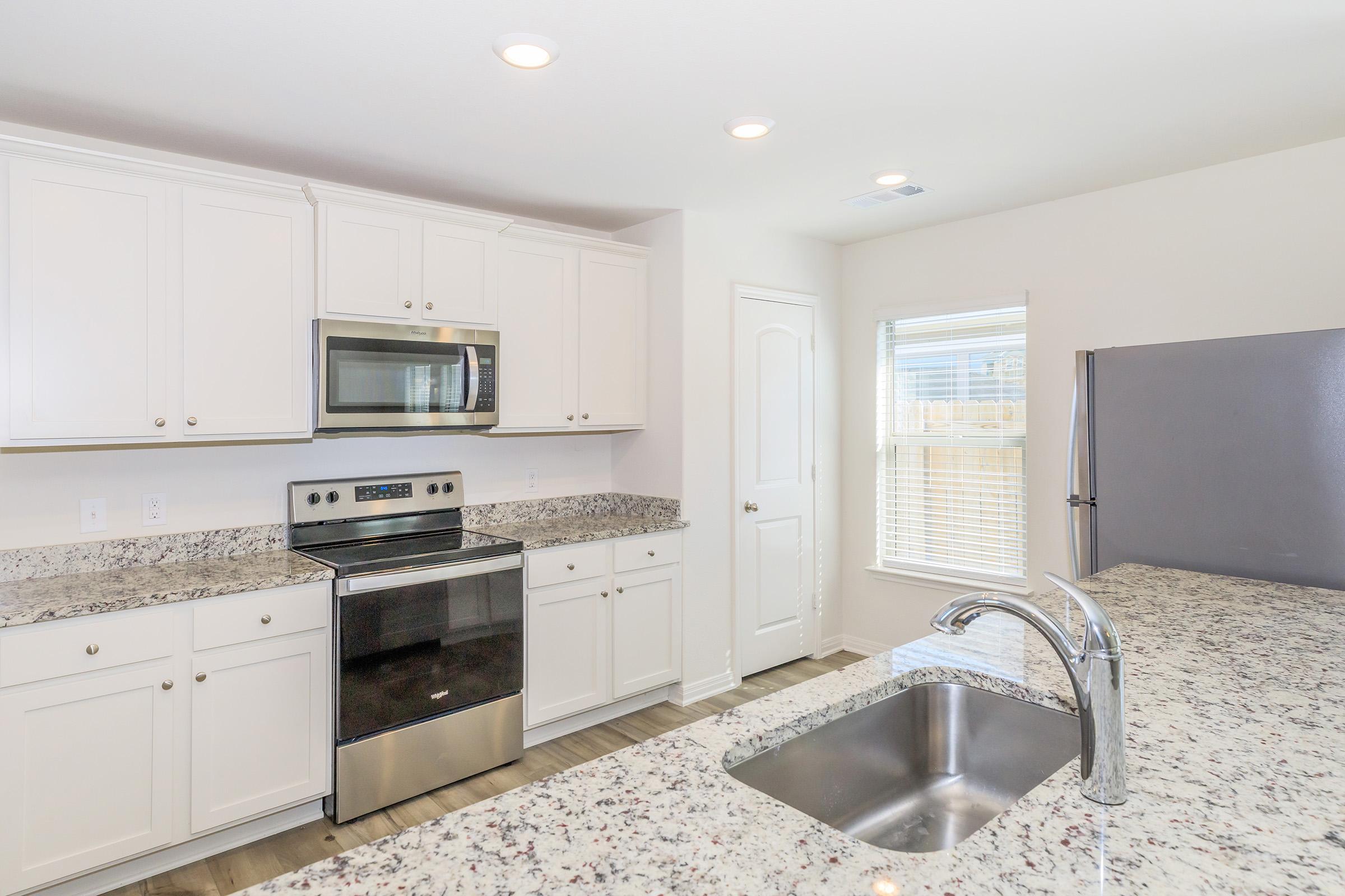 Modern kitchen featuring white cabinets, stainless steel appliances, and a granite countertop. The space includes an oven, microwave, and a side-by-side refrigerator, with a window allowing natural light to brighten the area. The sink is integrated into the countertop, complementing the overall design.