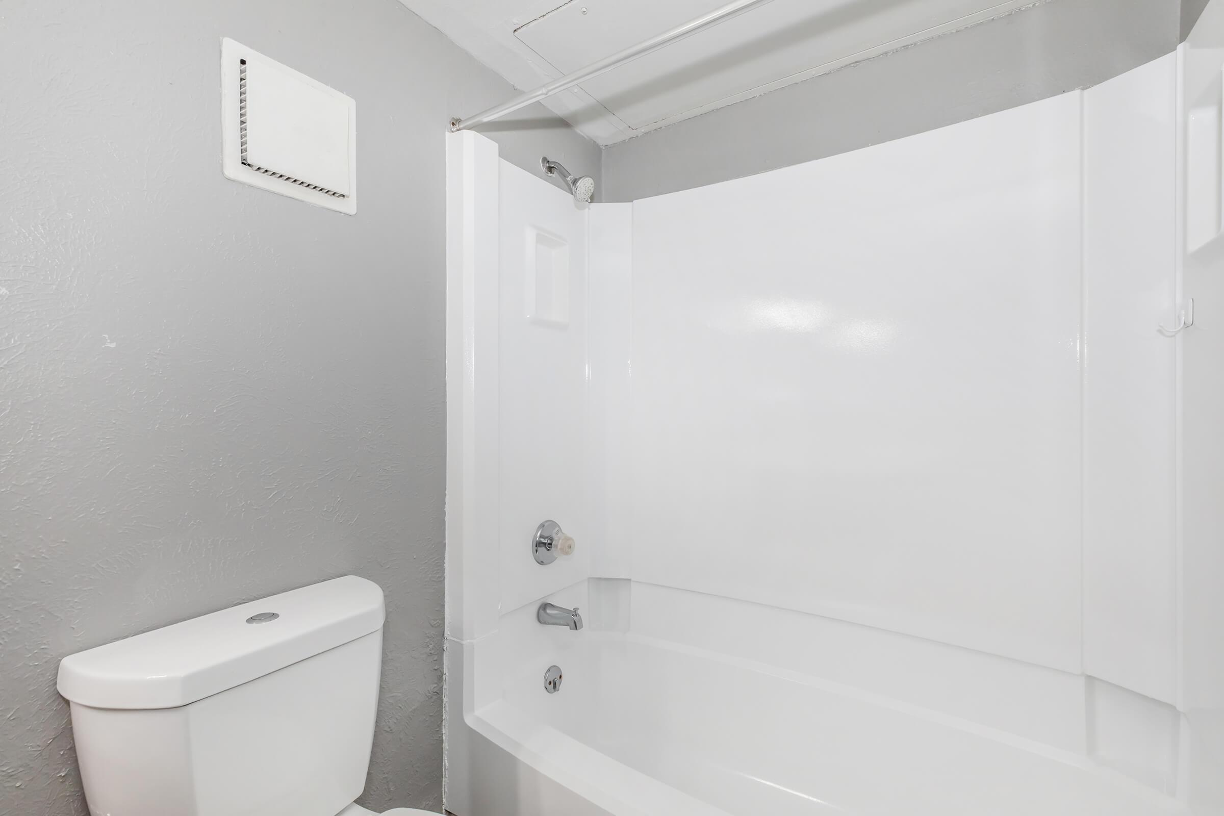 A bathroom featuring a white bathtub with a shower, a white toilet, and gray walls. The area is clean and well-lit, showcasing a simple design with minimal decor.