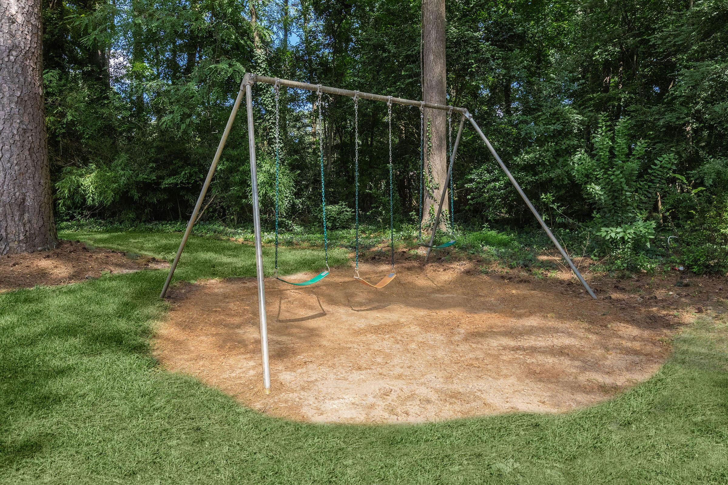 a swing set in a grassy area with trees in the background